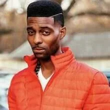 A young man with a short, high-top fade hairstyle, wearing a red jacket, looking at the camera with a neutral expression.