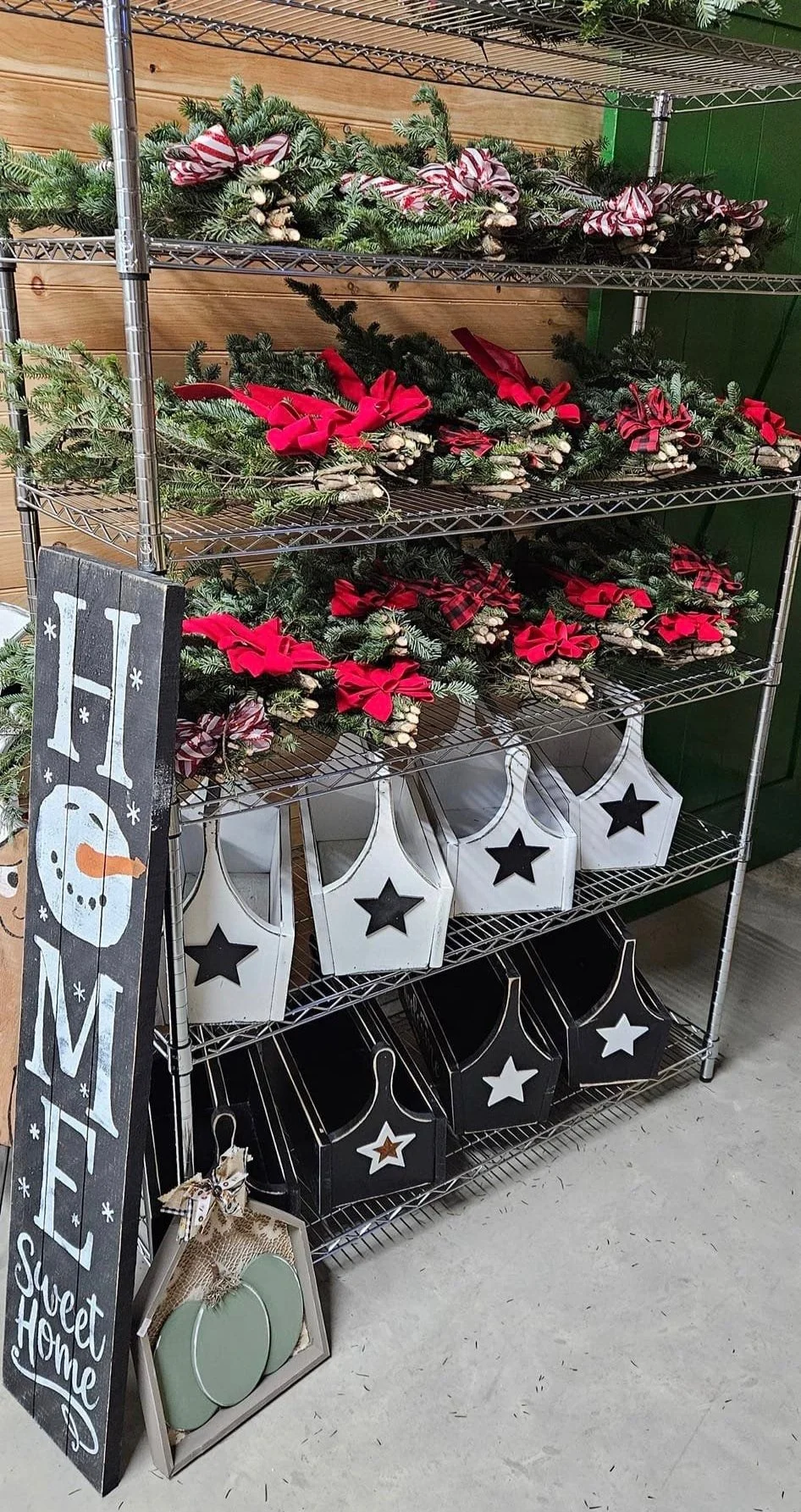 The photo shows a display of festive holiday decorations, including greenery with red bows, decorative lanterns with star cutouts, and a "Home Sweet Home" wooden sign.
