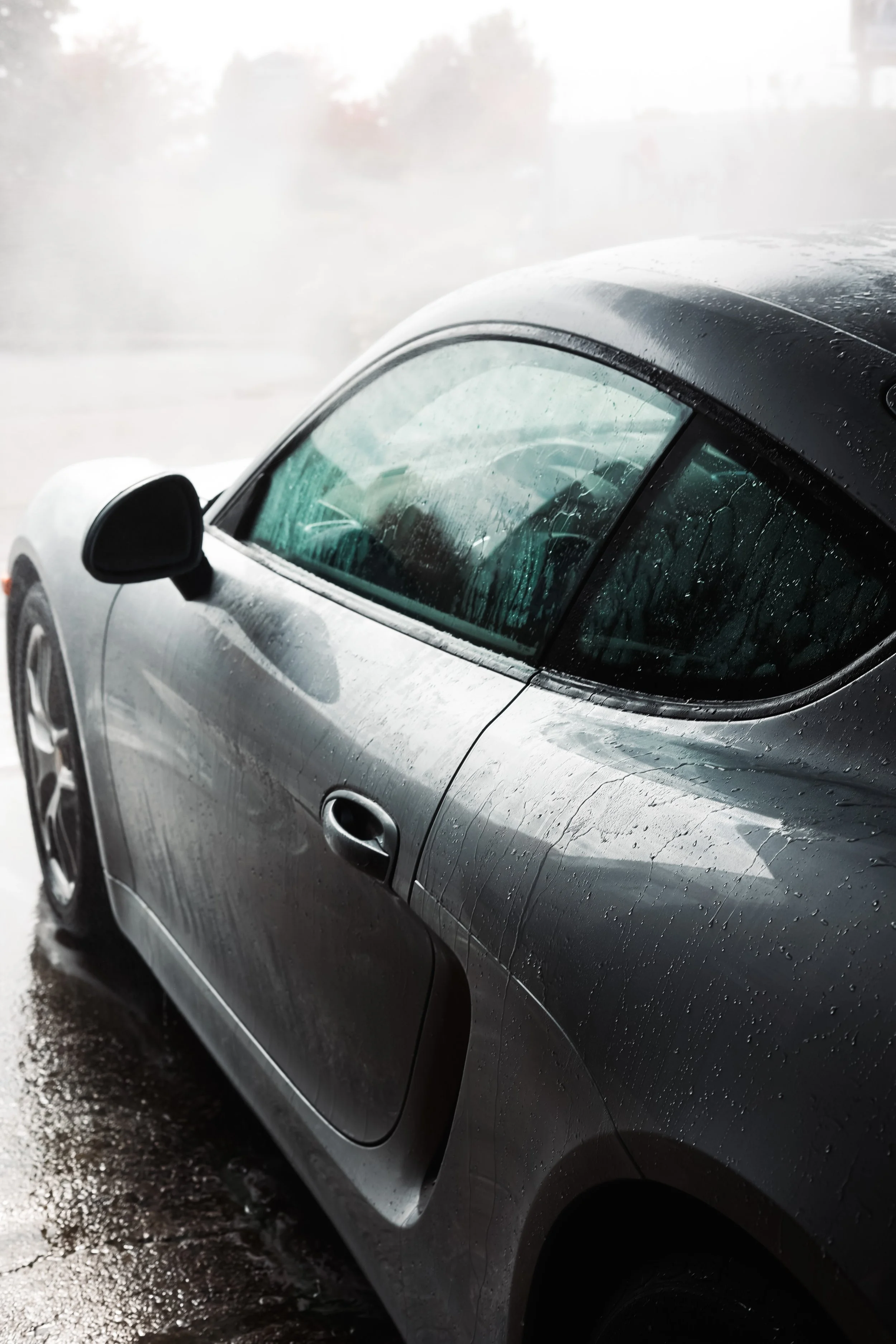 Side view of a wet grey sports car with water droplets on the windows and body, parked or moving indoors.