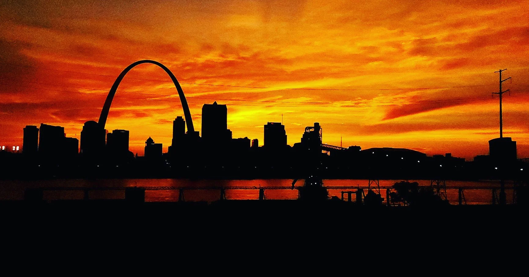 Silhouette of a city skyline with an arch during a vivid orange sunset