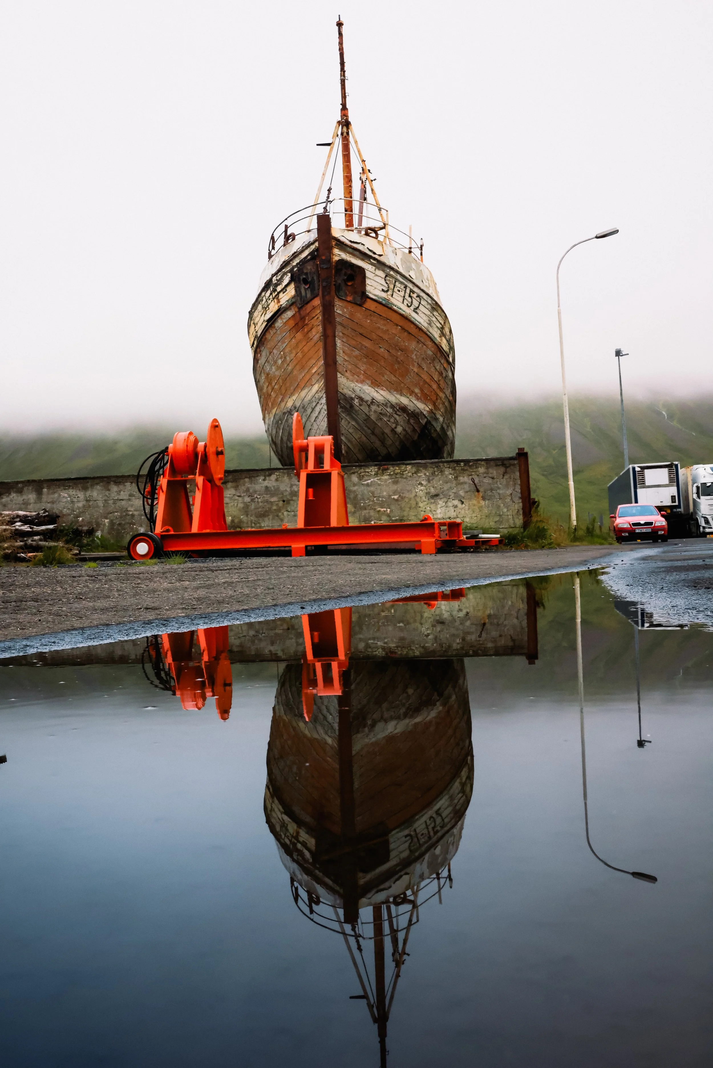 Old wooden boat on land with orange machinery and puddle reflection