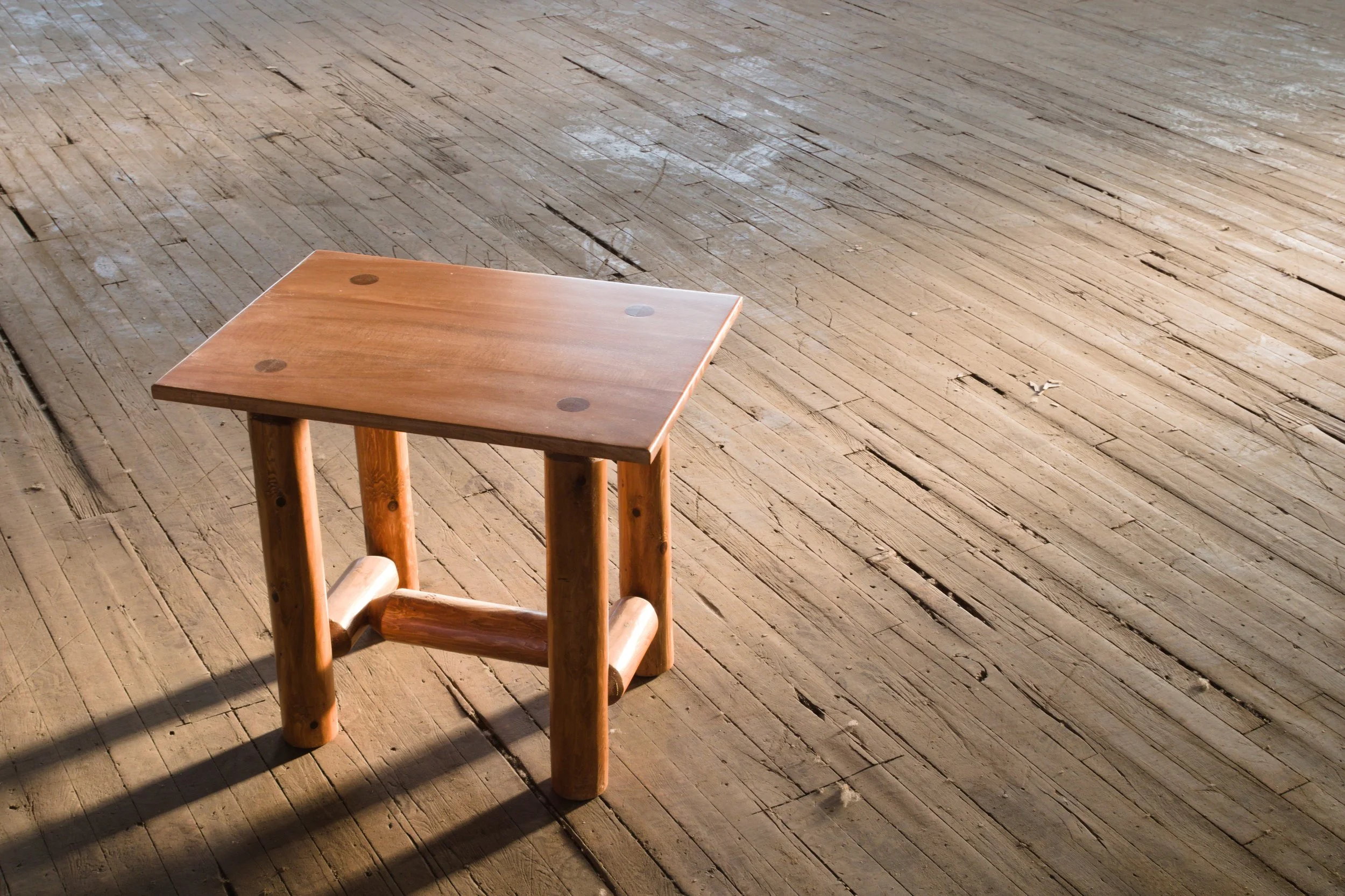 A small wooden stool with a square top on a wooden floor.