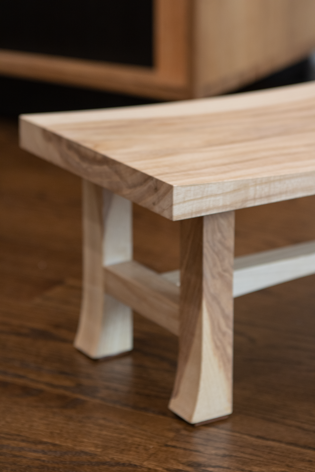 Close-up of a small wooden table or stool with angled legs, placed on a wooden floor.