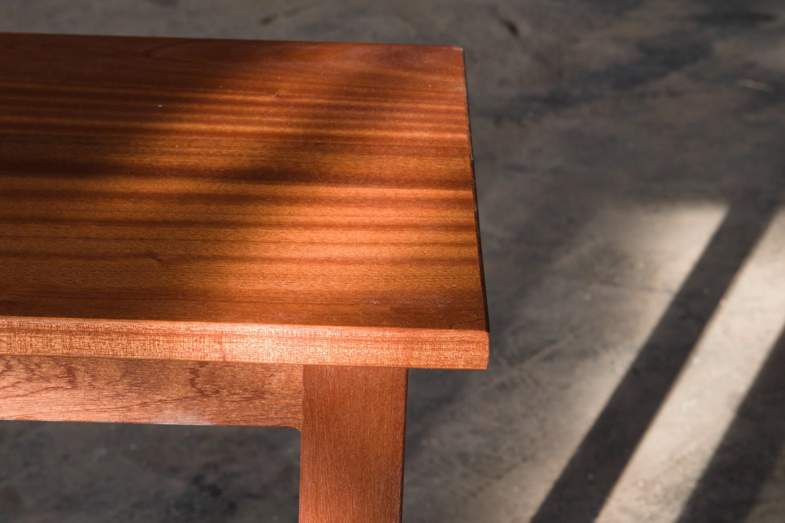 Close-up of a wooden table corner with a shadow cast on a concrete floor.