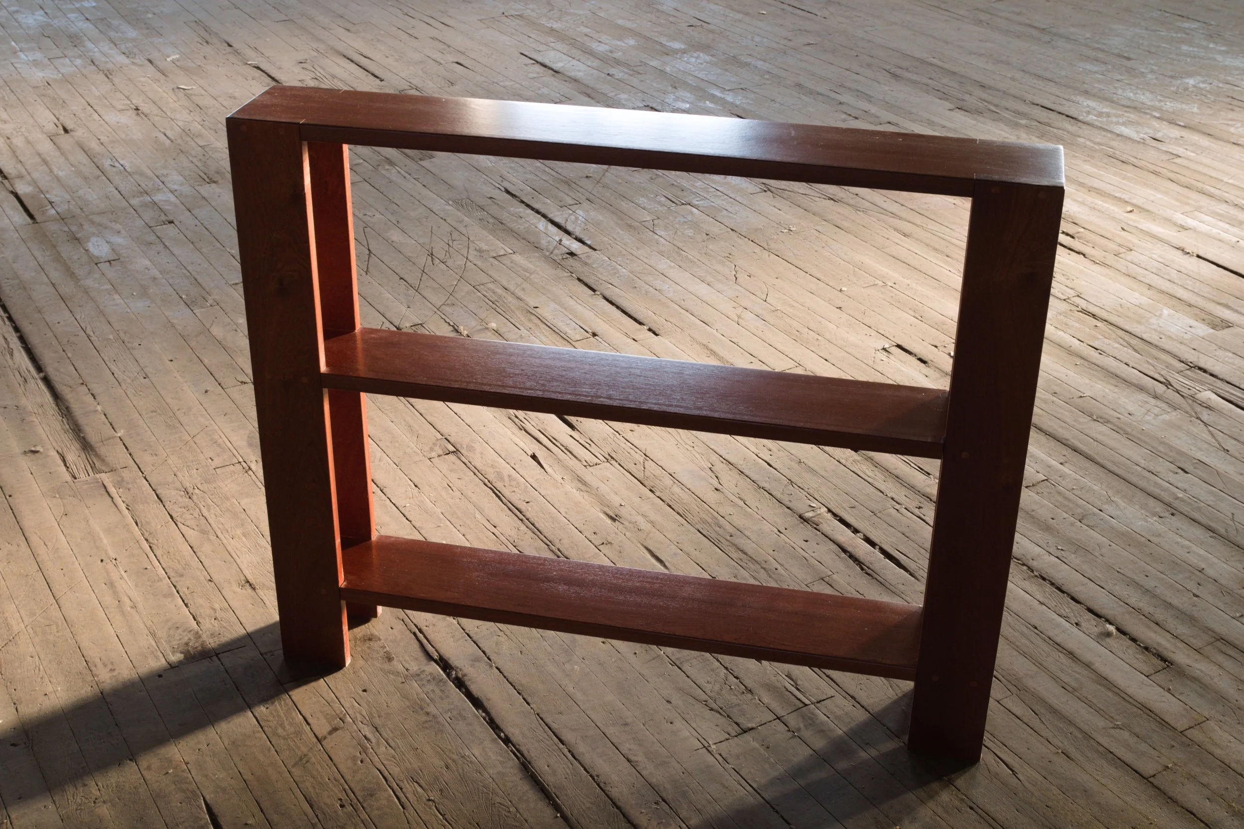 Wooden bookshelf with three shelves on a wooden floor.