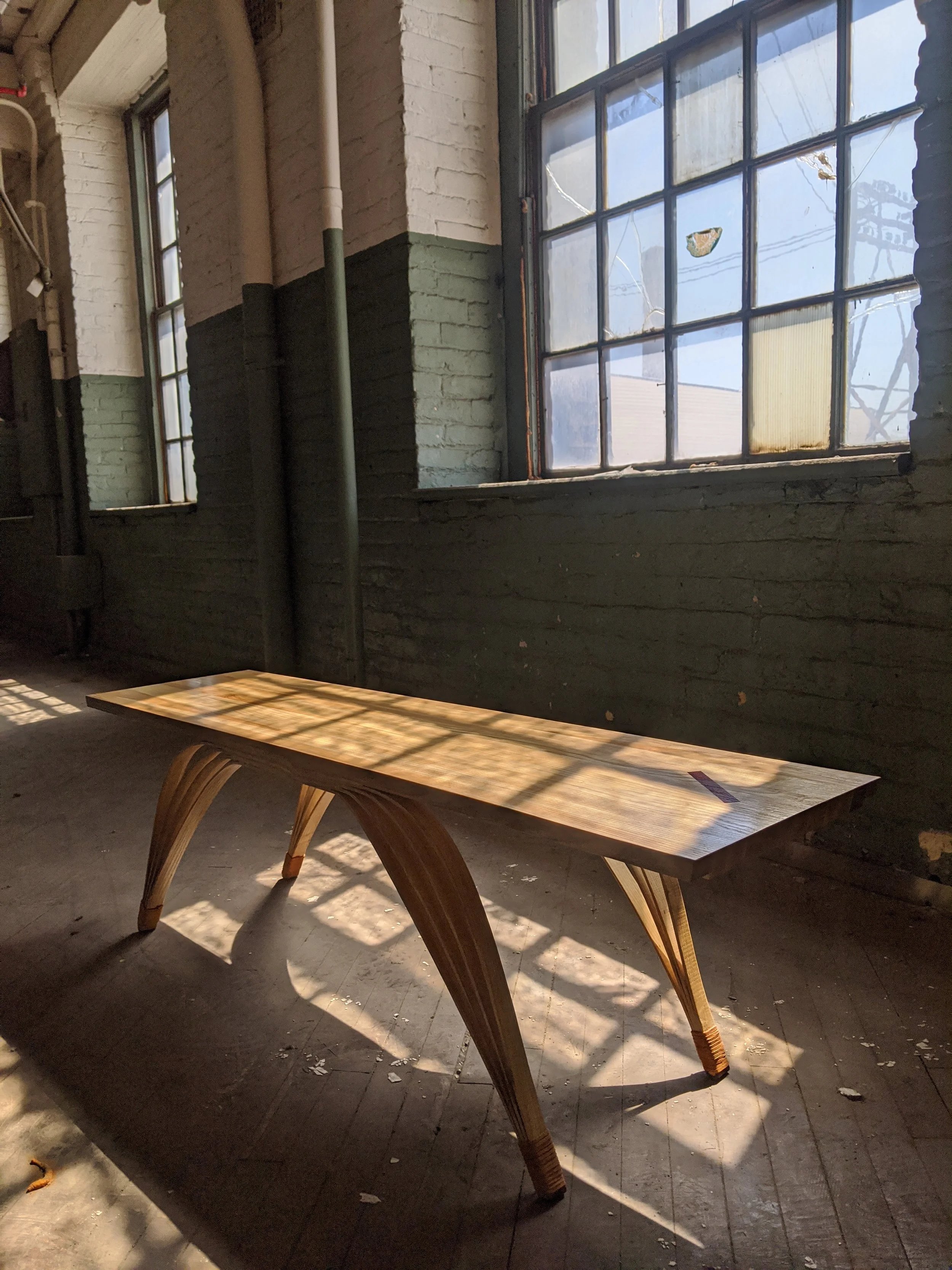 Sunlight streaming through a large industrial-style window, casting shadows on a wooden table, inside a rustic building with brick walls.