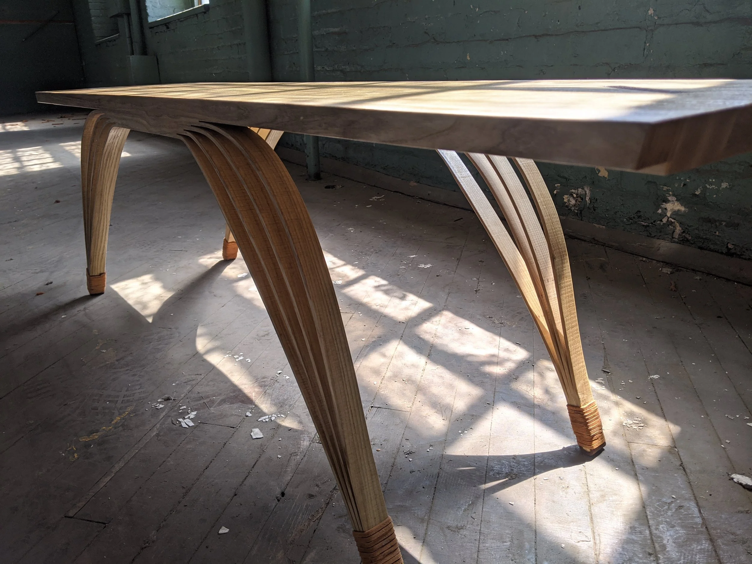 A wooden bench with curved legs on a wooden floor, illuminated by sunlight.