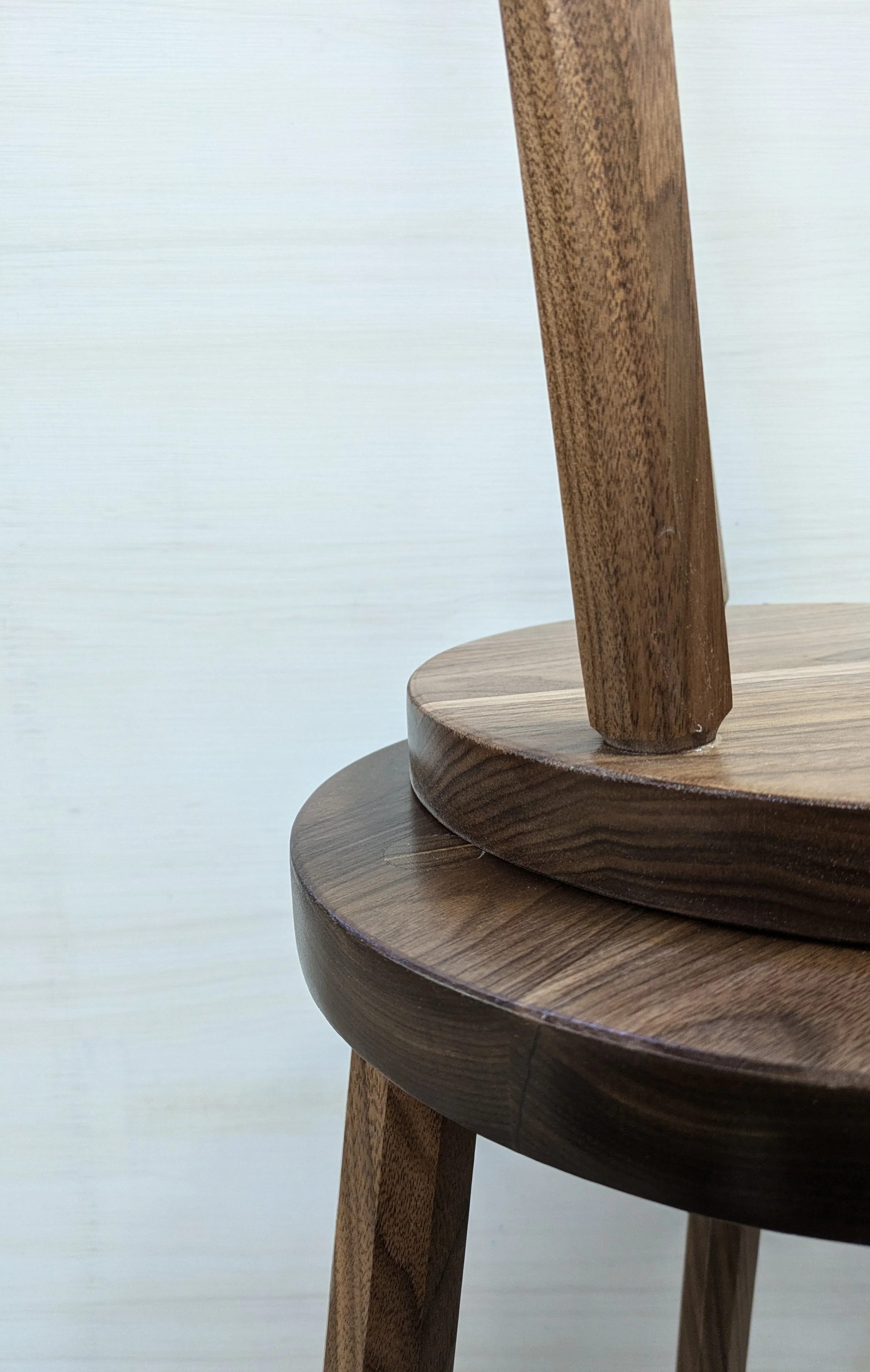 Close-up of a wooden chair showing the rounded seat and part of the back leg, made of dark wood.