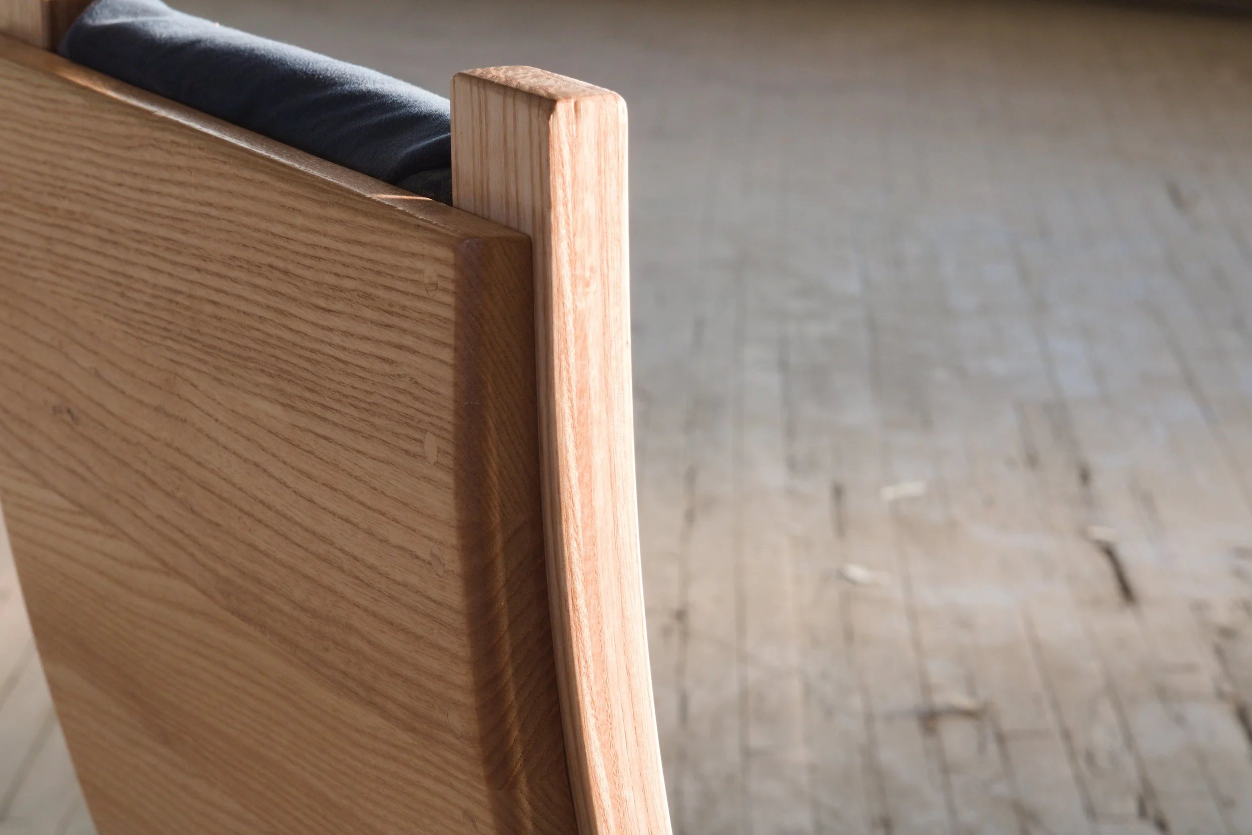 Close-up of a wooden piece joining the side of a wooden bed frame with a black mattress, on a wooden floor.
