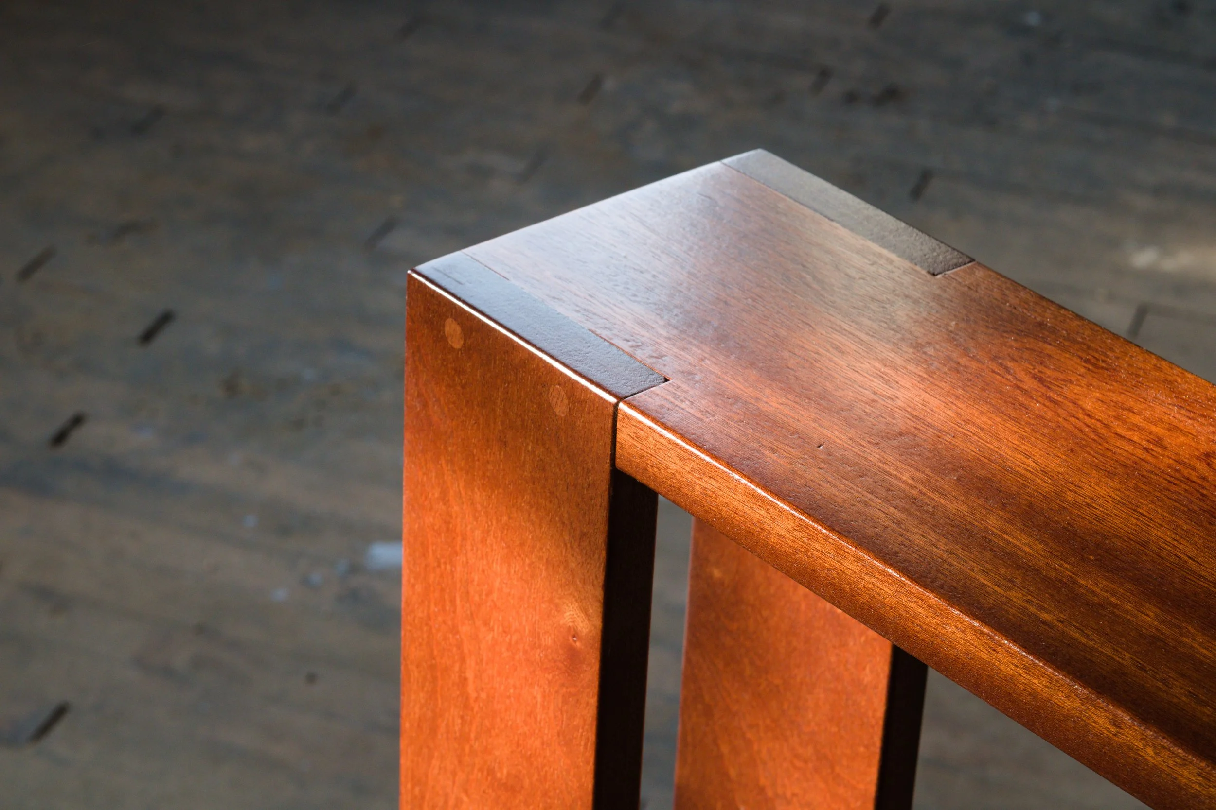 Close-up of the corner of a wooden table with warm brown finish, set against a dark wooden floor.