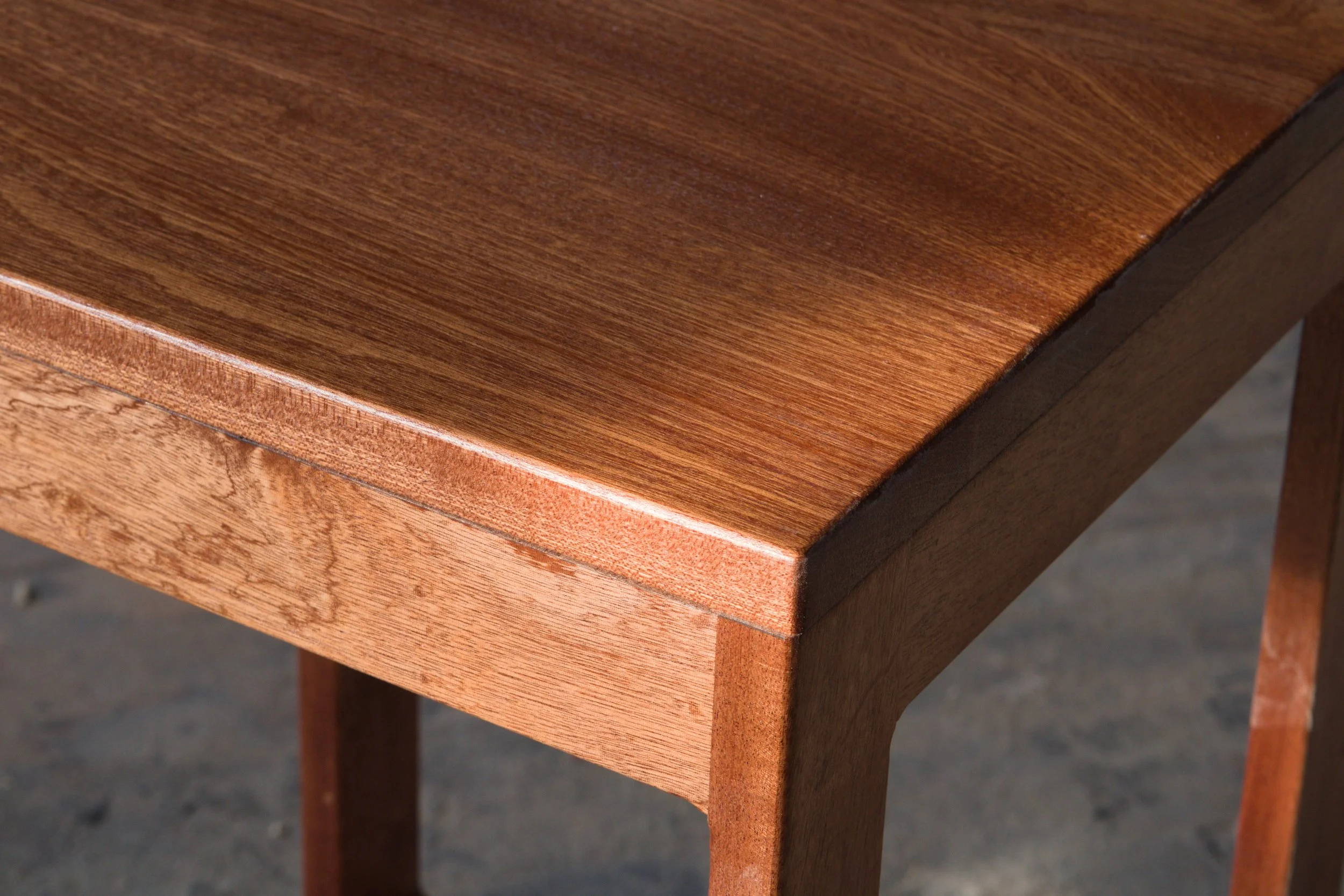 Close-up of a wooden table corner showing smooth, polished surface and beveled edge.