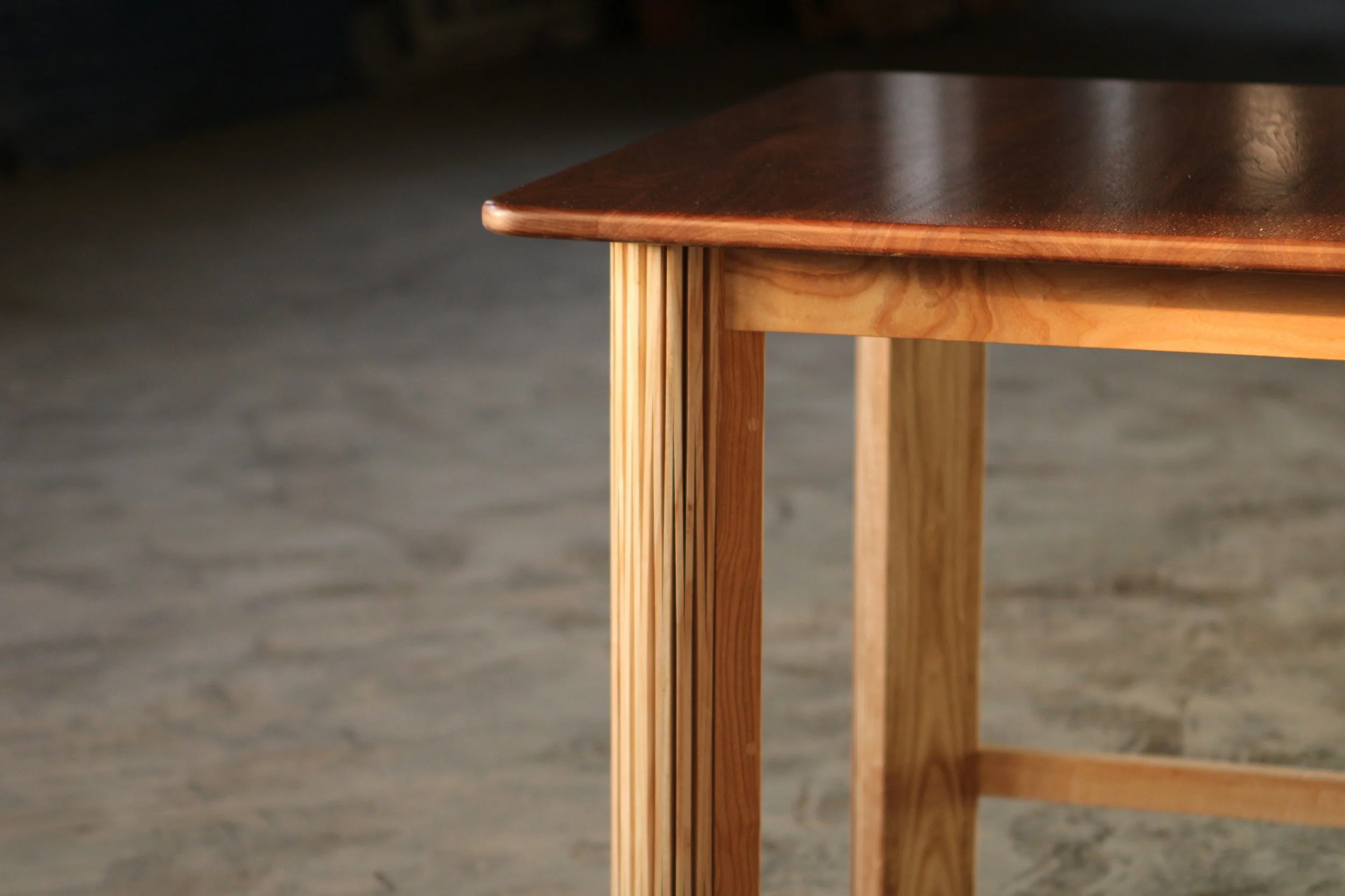 Close-up of a wooden table corner showing the rounded edge and wooden legs with visible wood grain.