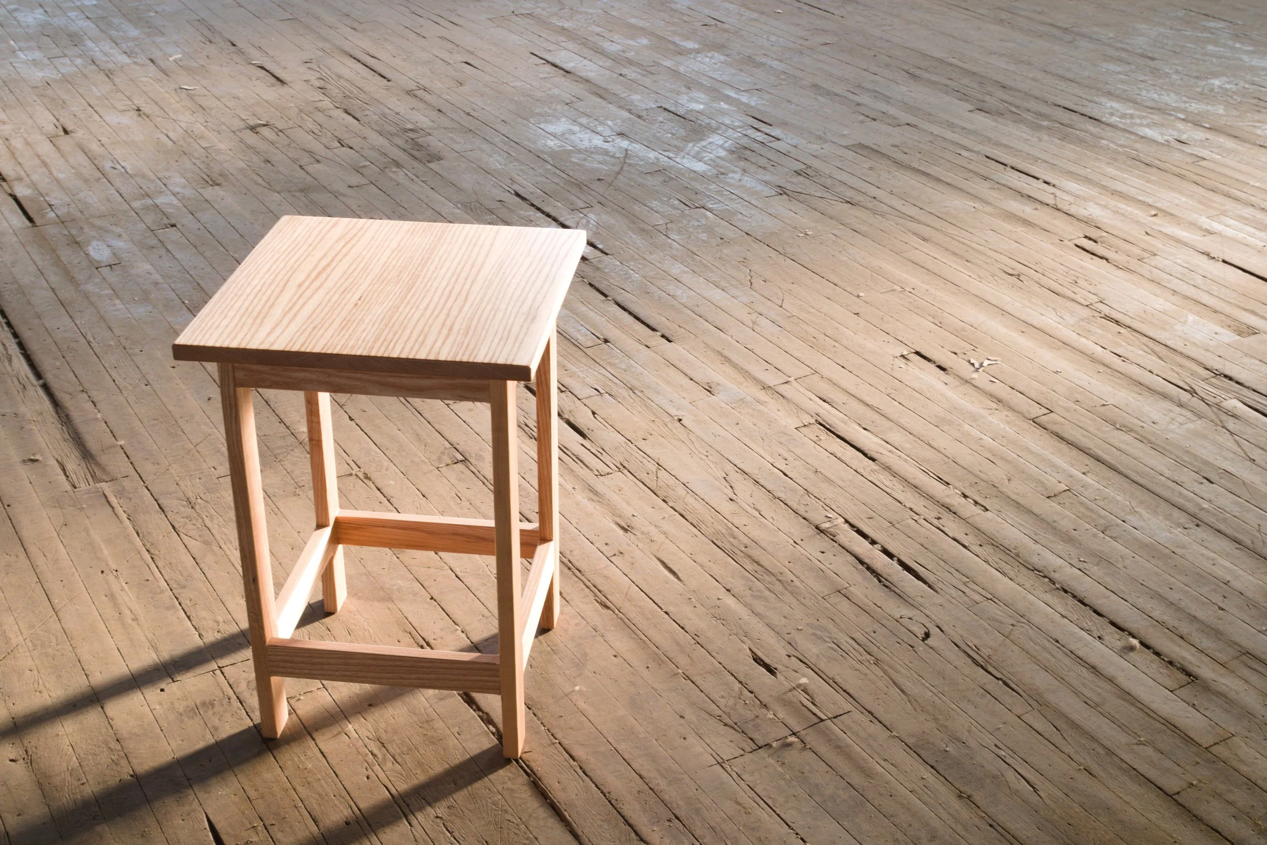 Empty wooden stool on a worn wooden floor.