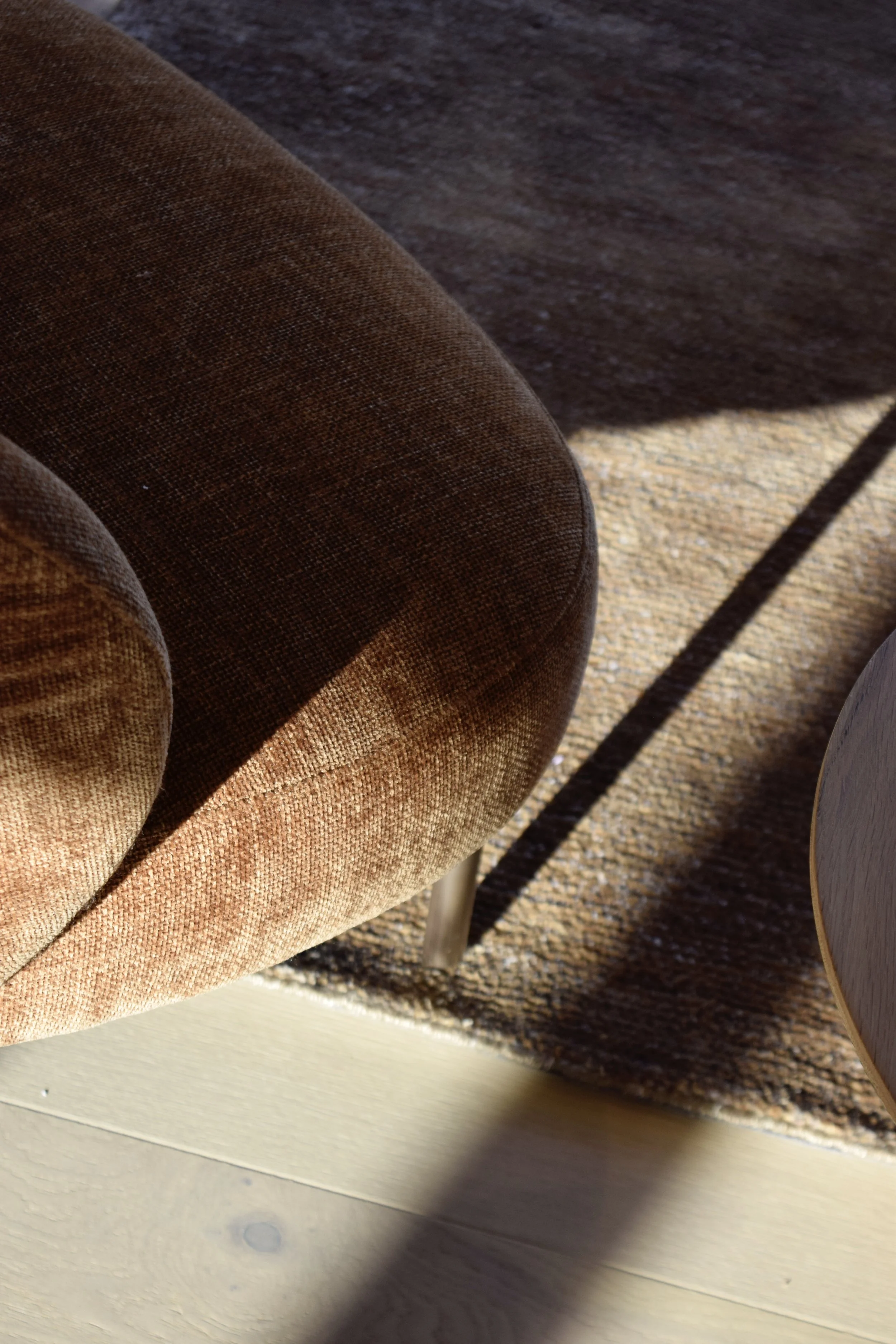 Close-up view of a brown upholstered chair with thin metal legs, placed on a light-colored wooden floor and a textured brown rug.