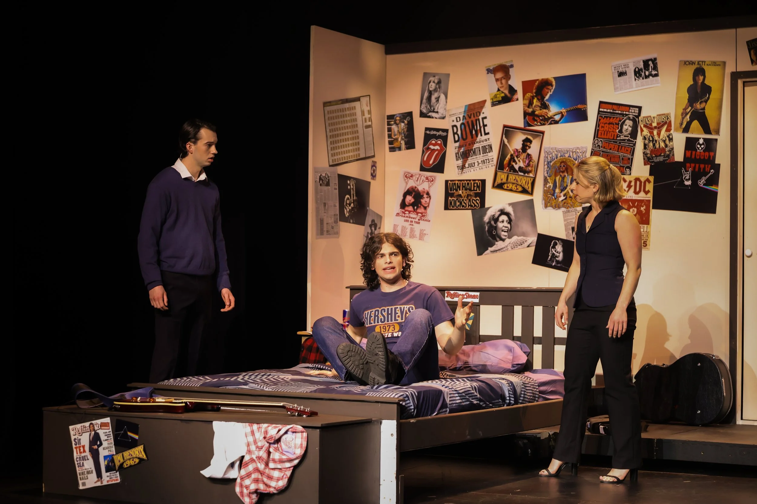 Production photo from School of Rock featuring Dewey being woken up in bed by Ned and Patty during the comedic opening scene. Theatrical lighting, character interaction, and high-quality musical theatre photography at the National Theatre