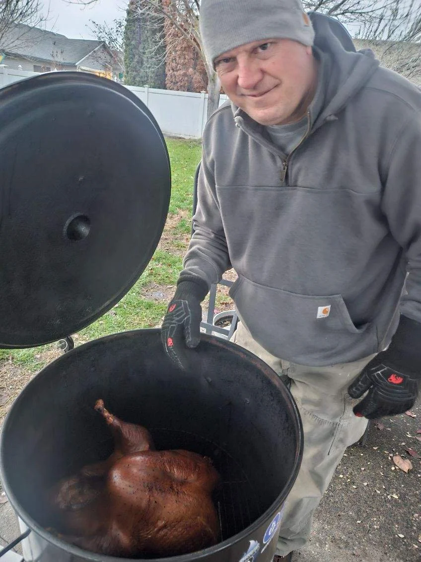 Pit-Matt-ster, Matt Morgan, outdoors next to a barrel smoker. Inside the smoker, a whole turkey is resting on a rack to celebrate Thanksgiving.