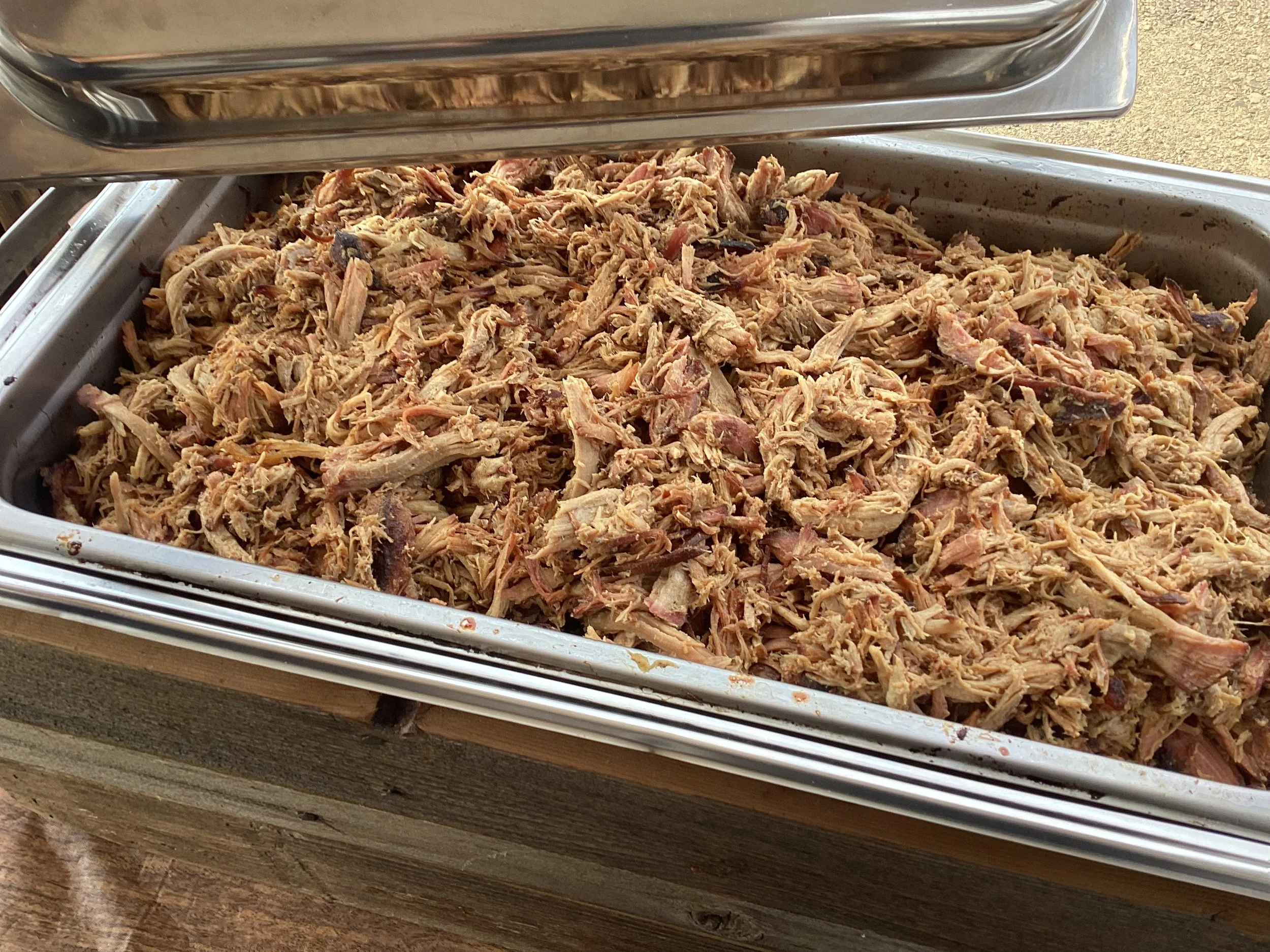 A stainless steel tray filled with smoked pulled pork meat for catering event.