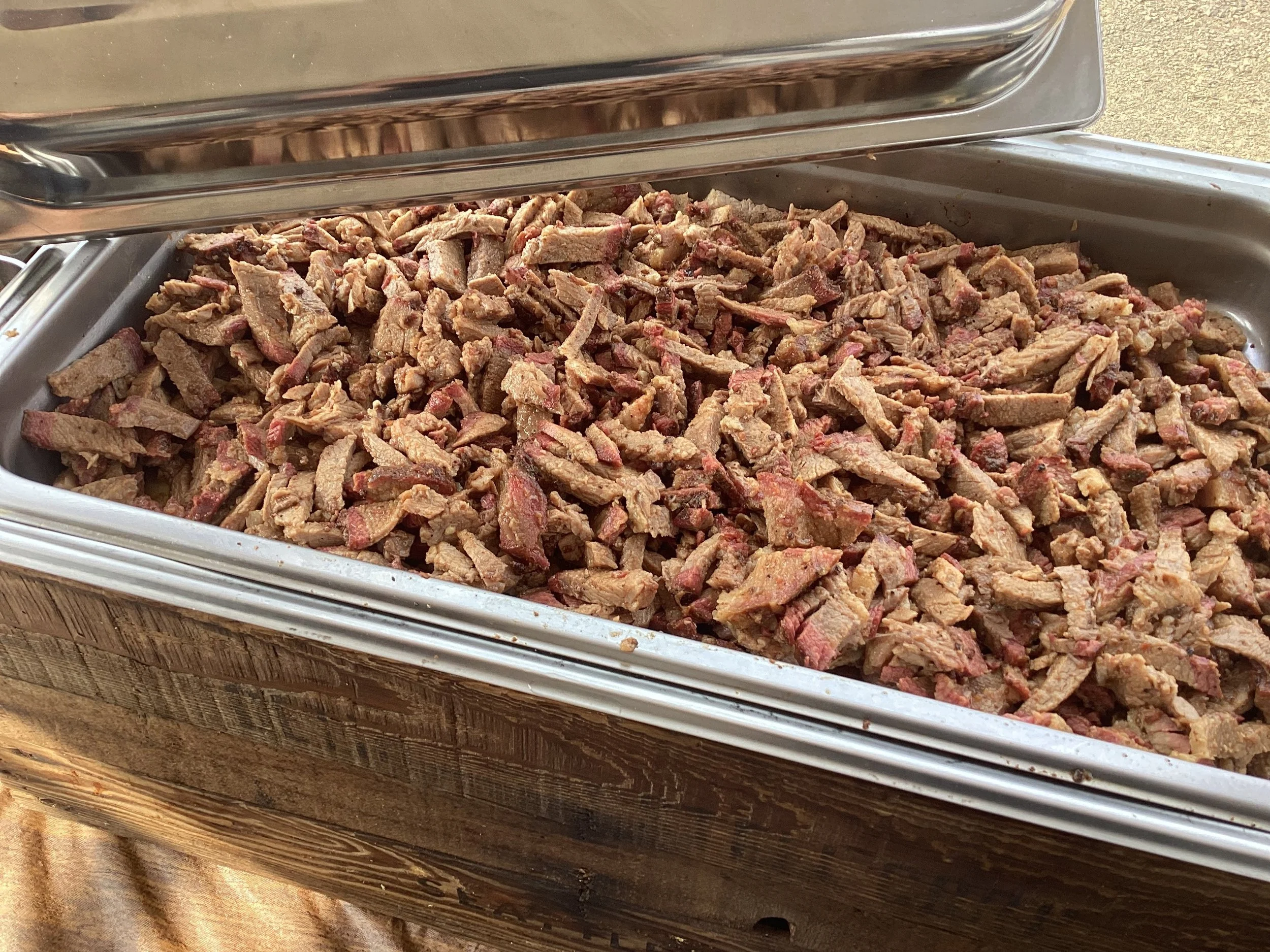 A stainless steel tray filled with chopped smoked beef brisket for catering event.