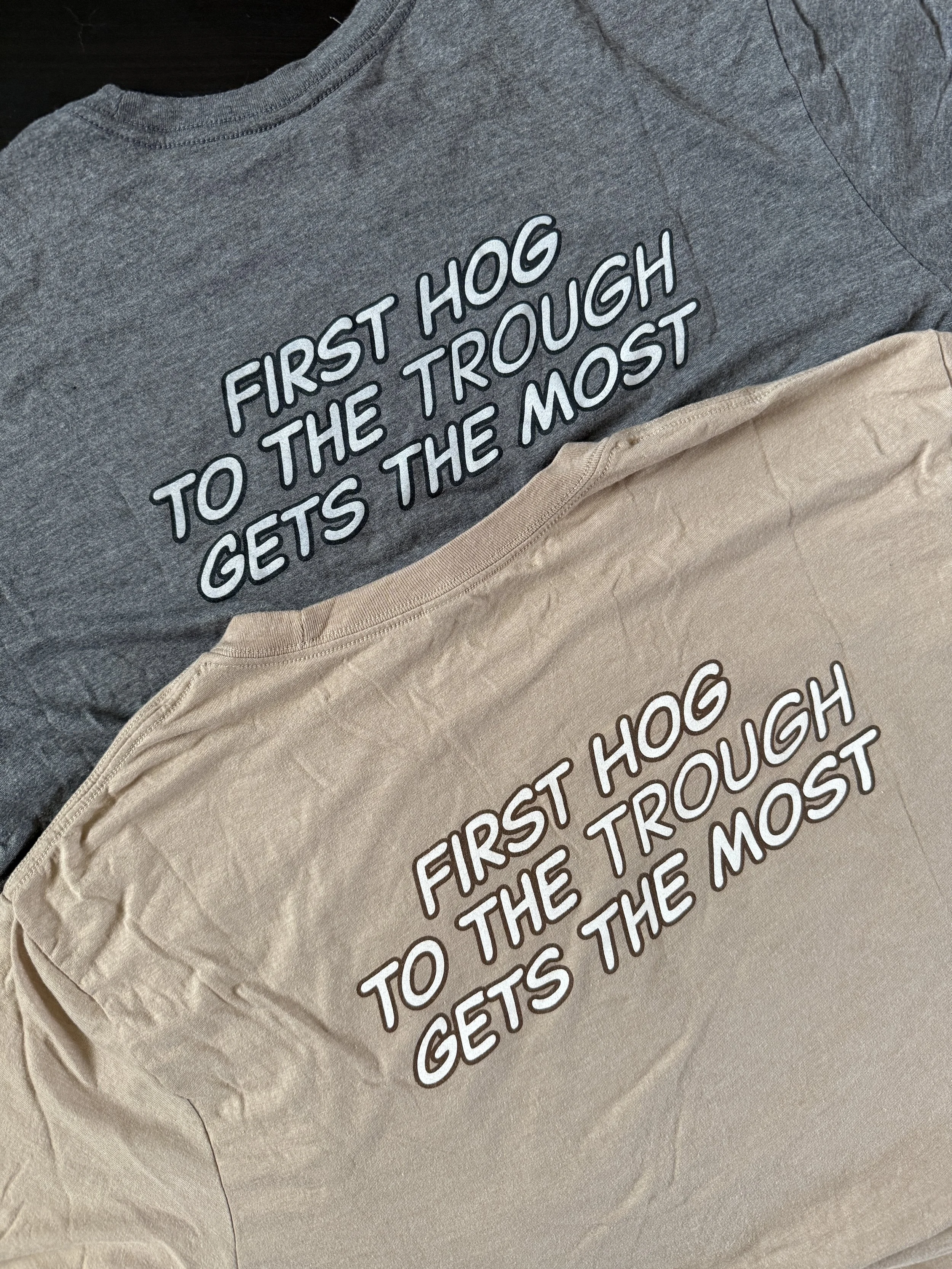 Blind Duck BBQ t-shirts with the printed message on the back: "First hog to the trough gets the most"; one t-shirt gray, the other tan.