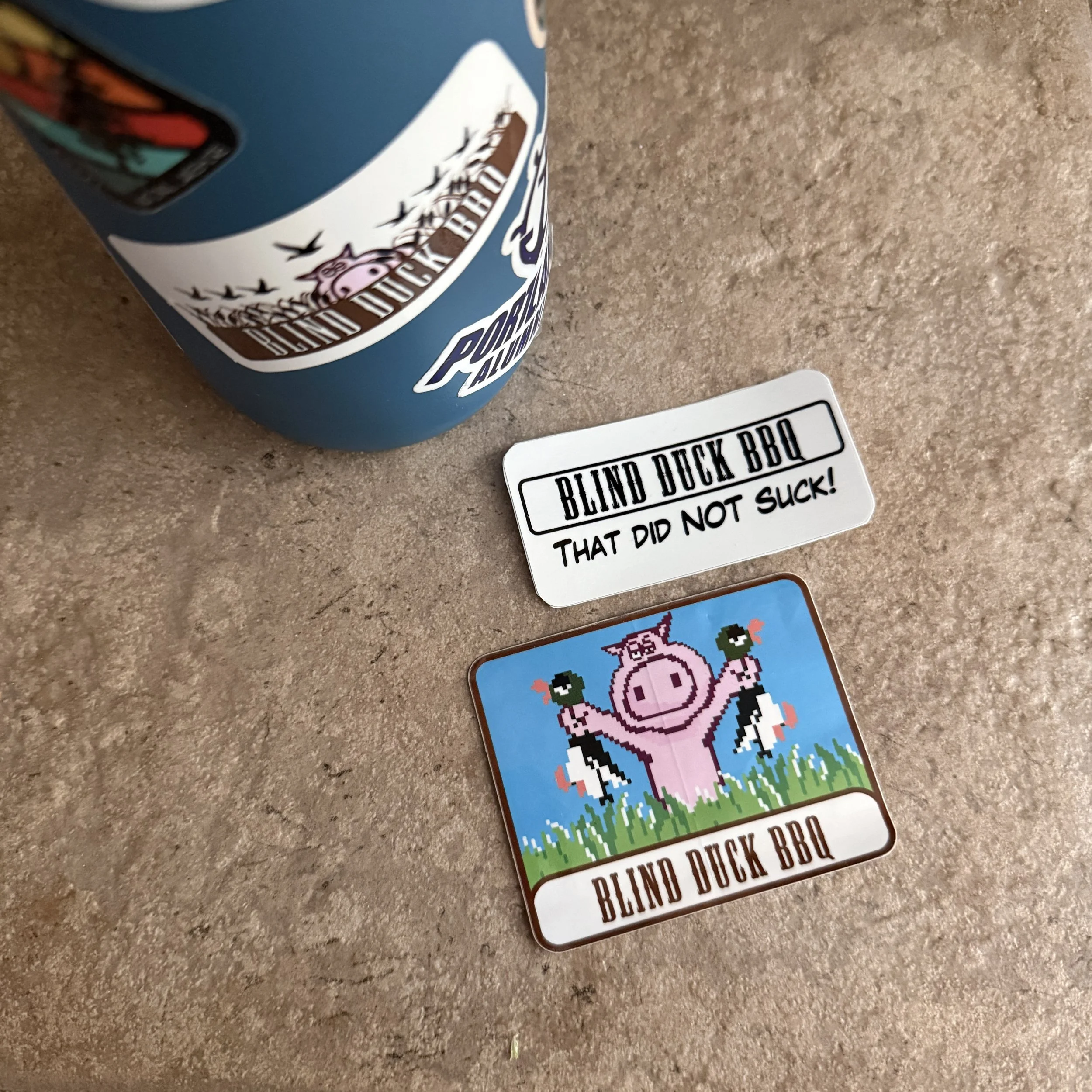 Three white rectangular Blind Duck BBQ sticker designs with the company logo and fun BBQ related graphics.