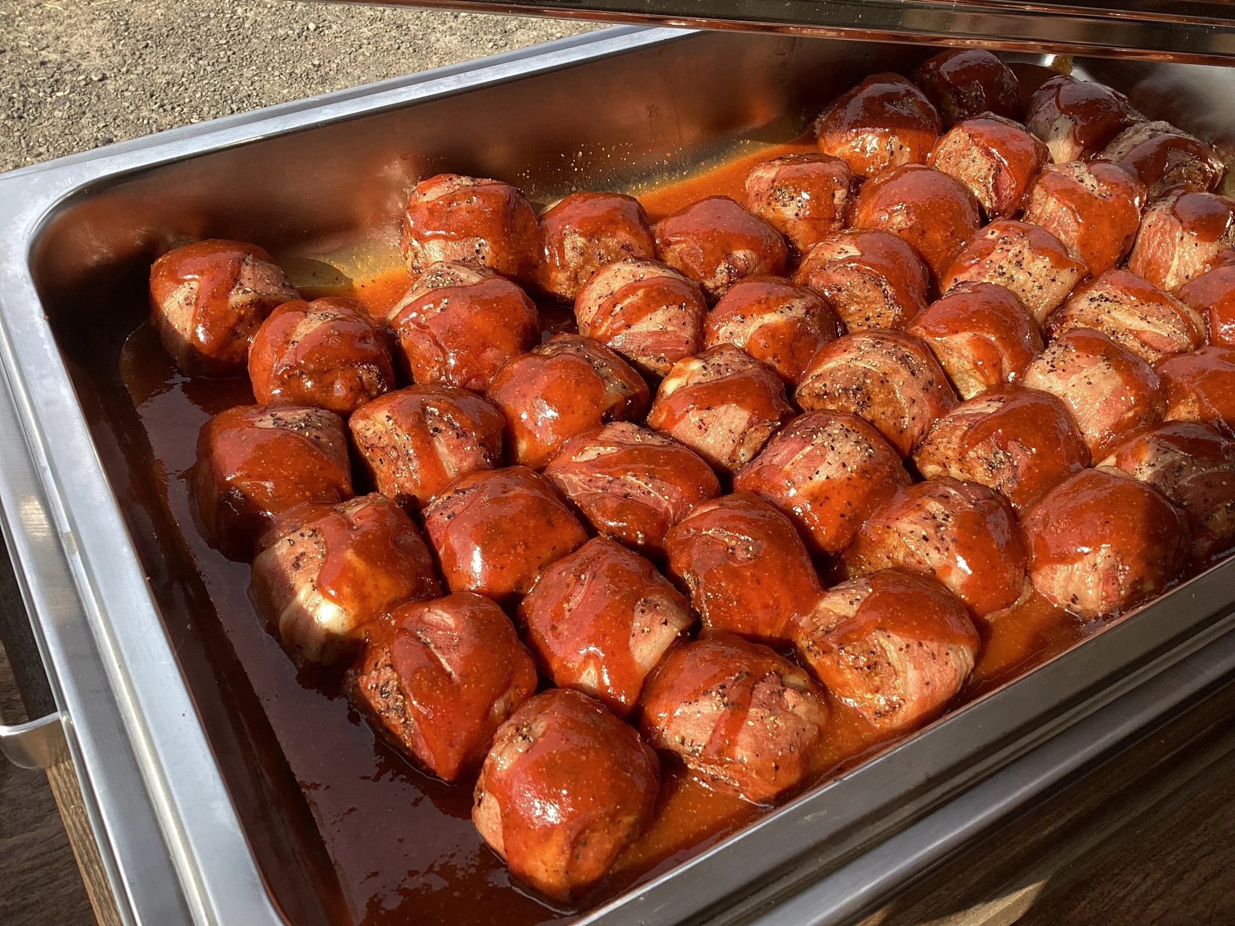 A stainless steel tray filled with Blind Duck BBQ famous Hog Ballz (cheese stuffed, bacon wrapped, pork sausage meatballs) for catering event.