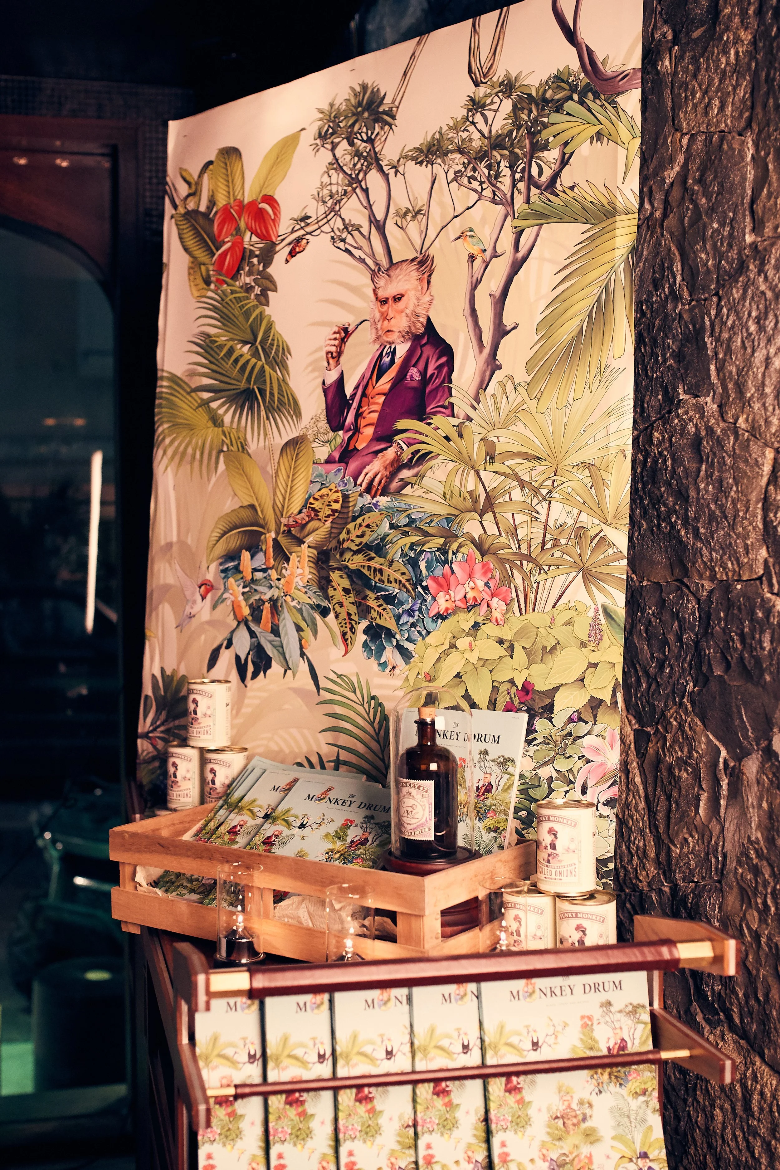 Decorative poster featuring an anthropomorphic monkey with a lion's head dressed in a purple suit, seated among tropical plants, with product displays and magazines titled 'Monkey Drum' in the foreground.