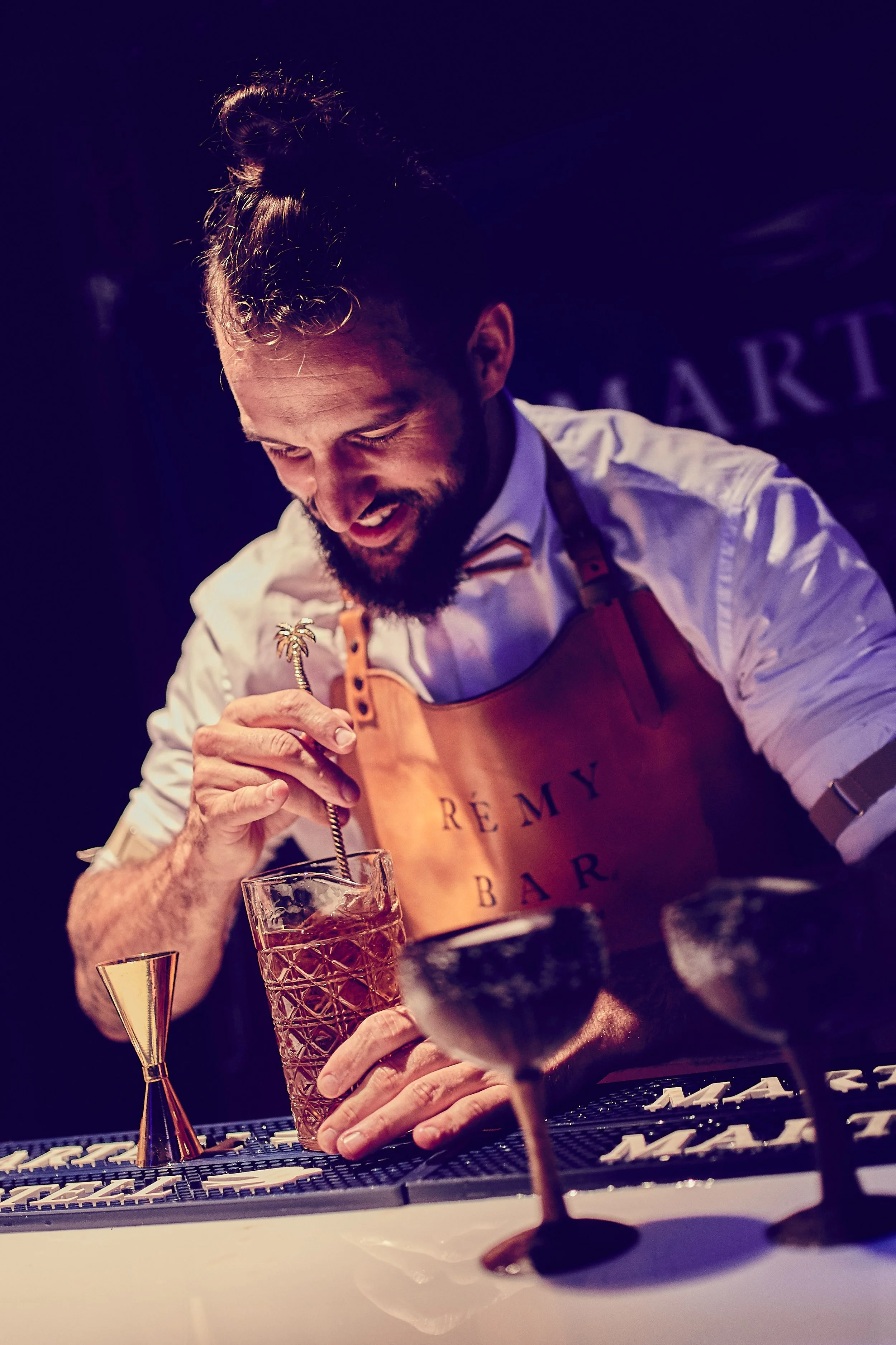 A bartender wearing a tan apron and white shirt preparing a drink.