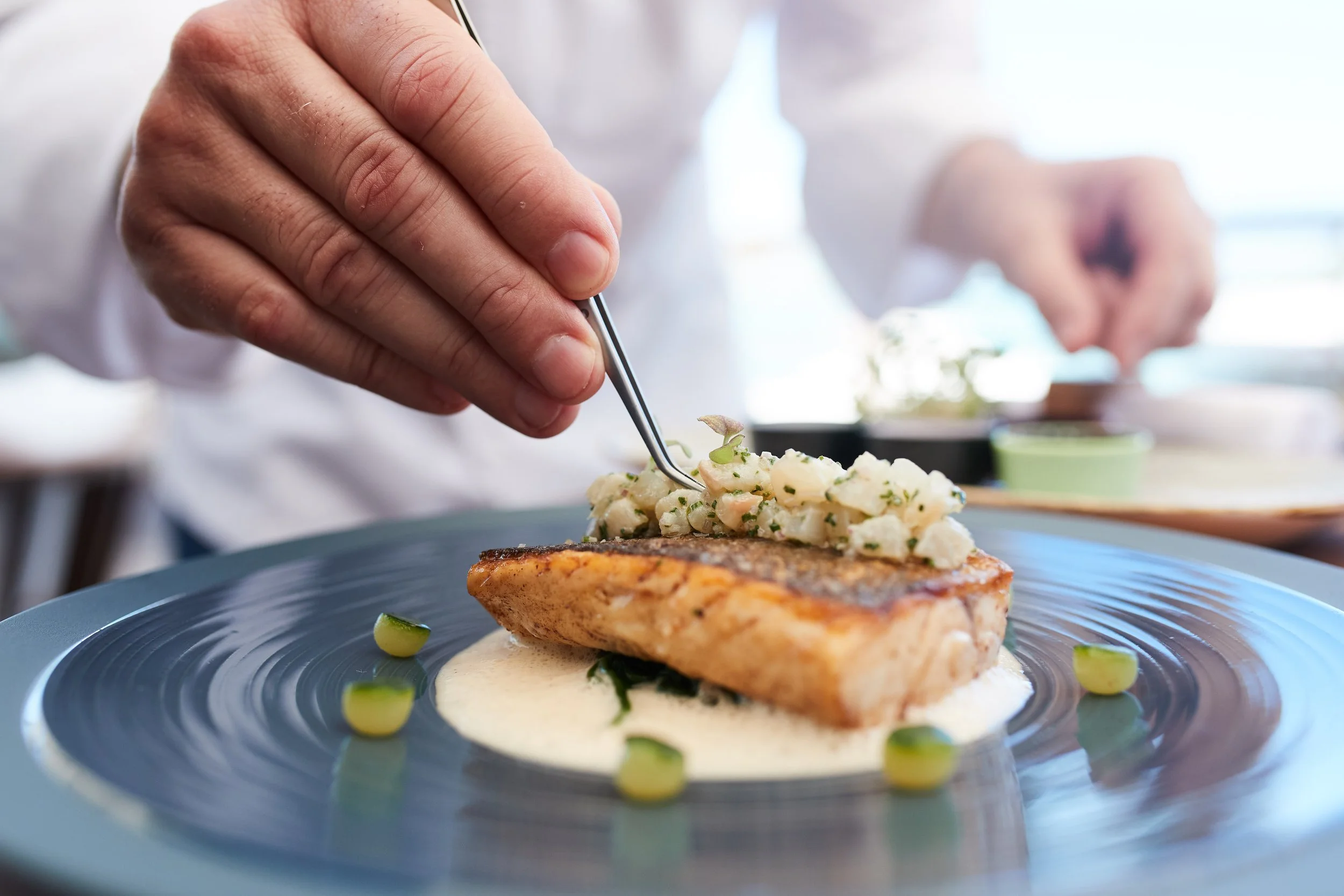 Chef garnishing a plated fish dish with herbs and sauce