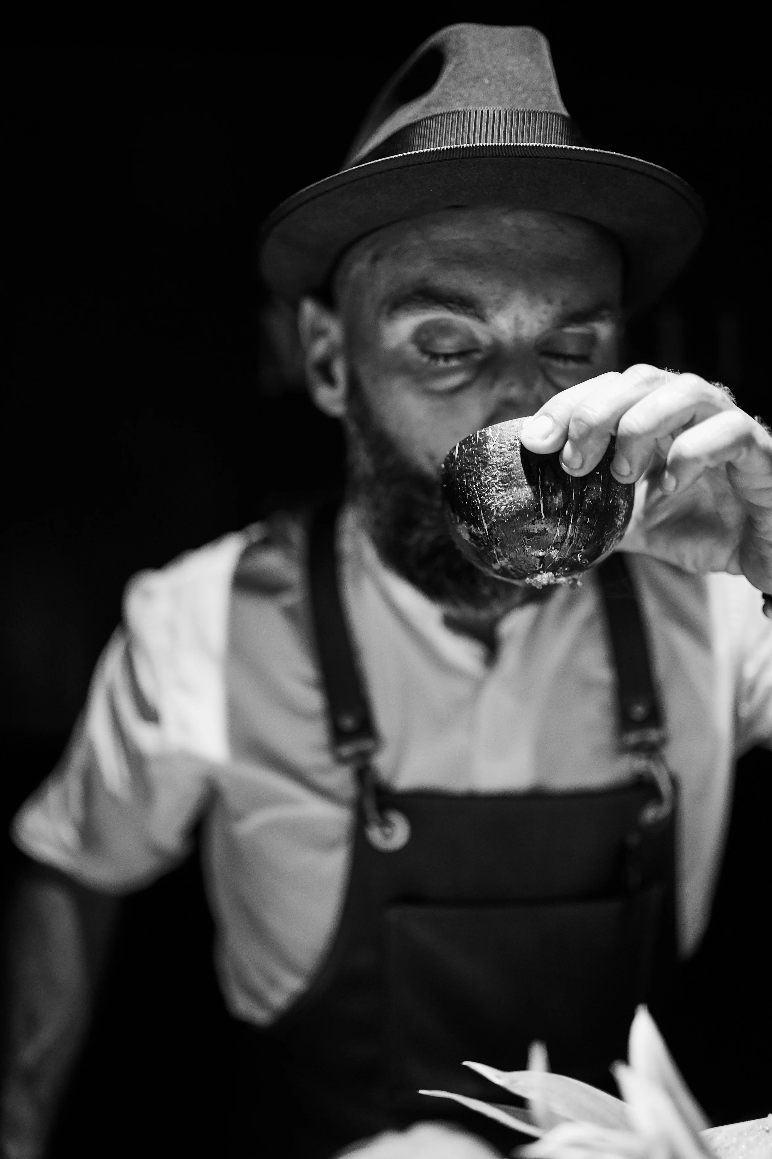 Black and white photo of a man wearing a hat and apron, drinking from a bowl.