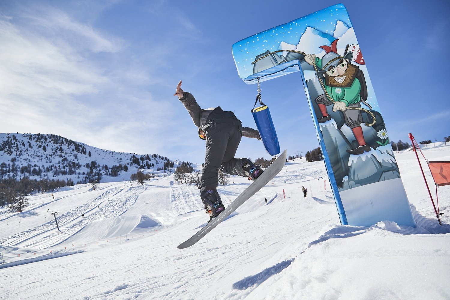 Snowboarder performing a trick beside a snow-park feature — photograph by Michaël Gramm