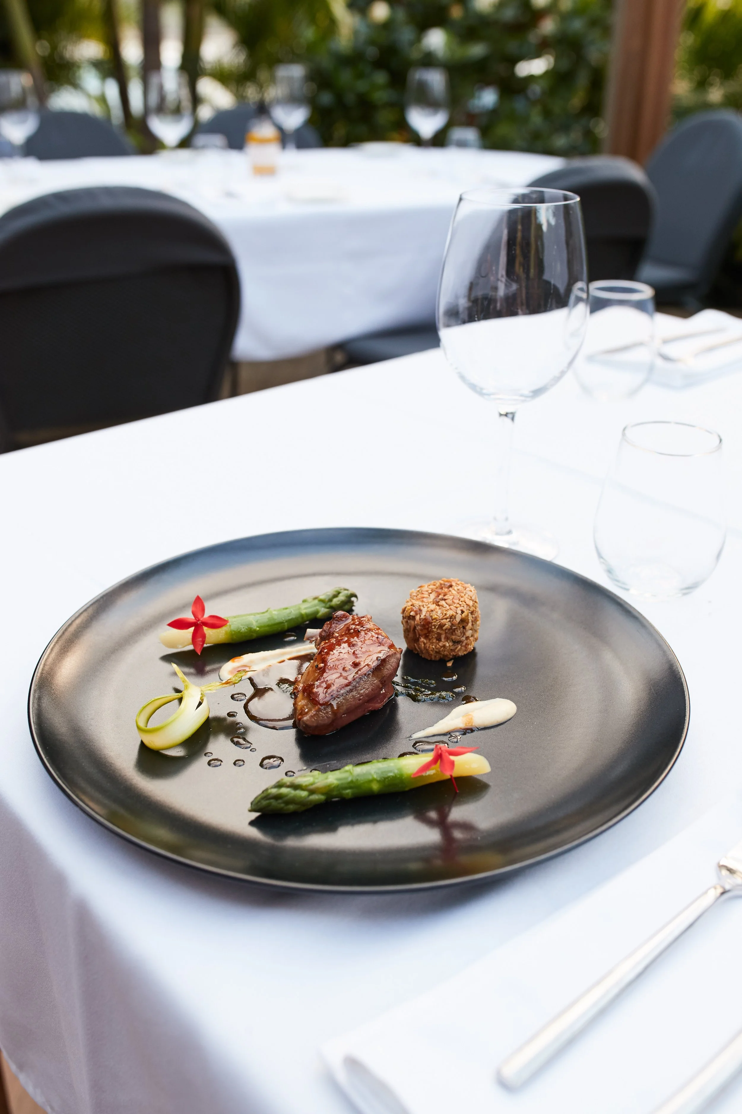 Elegant plate with cooked meat, asparagus, and garnishes on a white tablecloth at a fine dining restaurant.