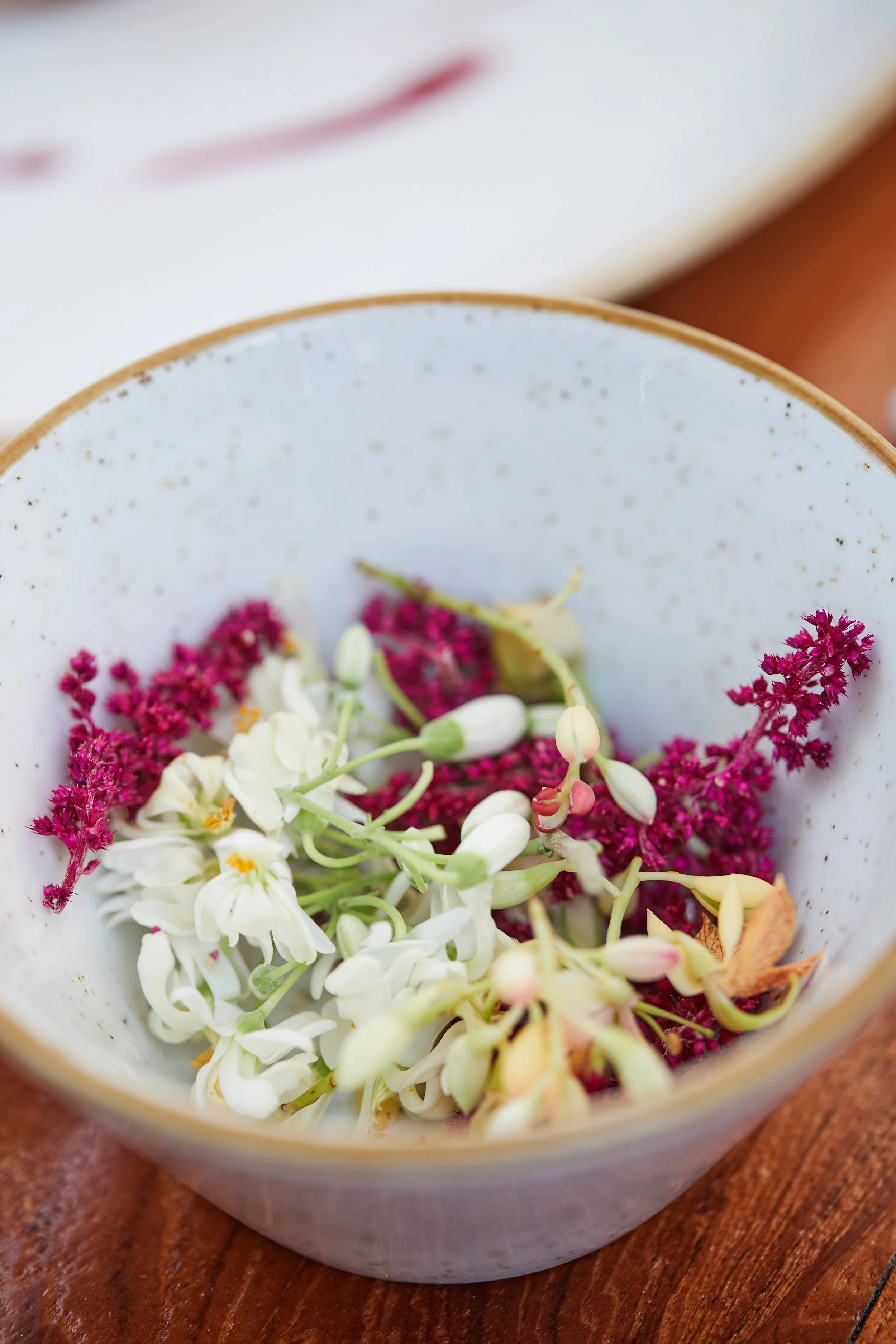 A white ceramic bowl filled with fresh white and purple flowers on a wooden surface.