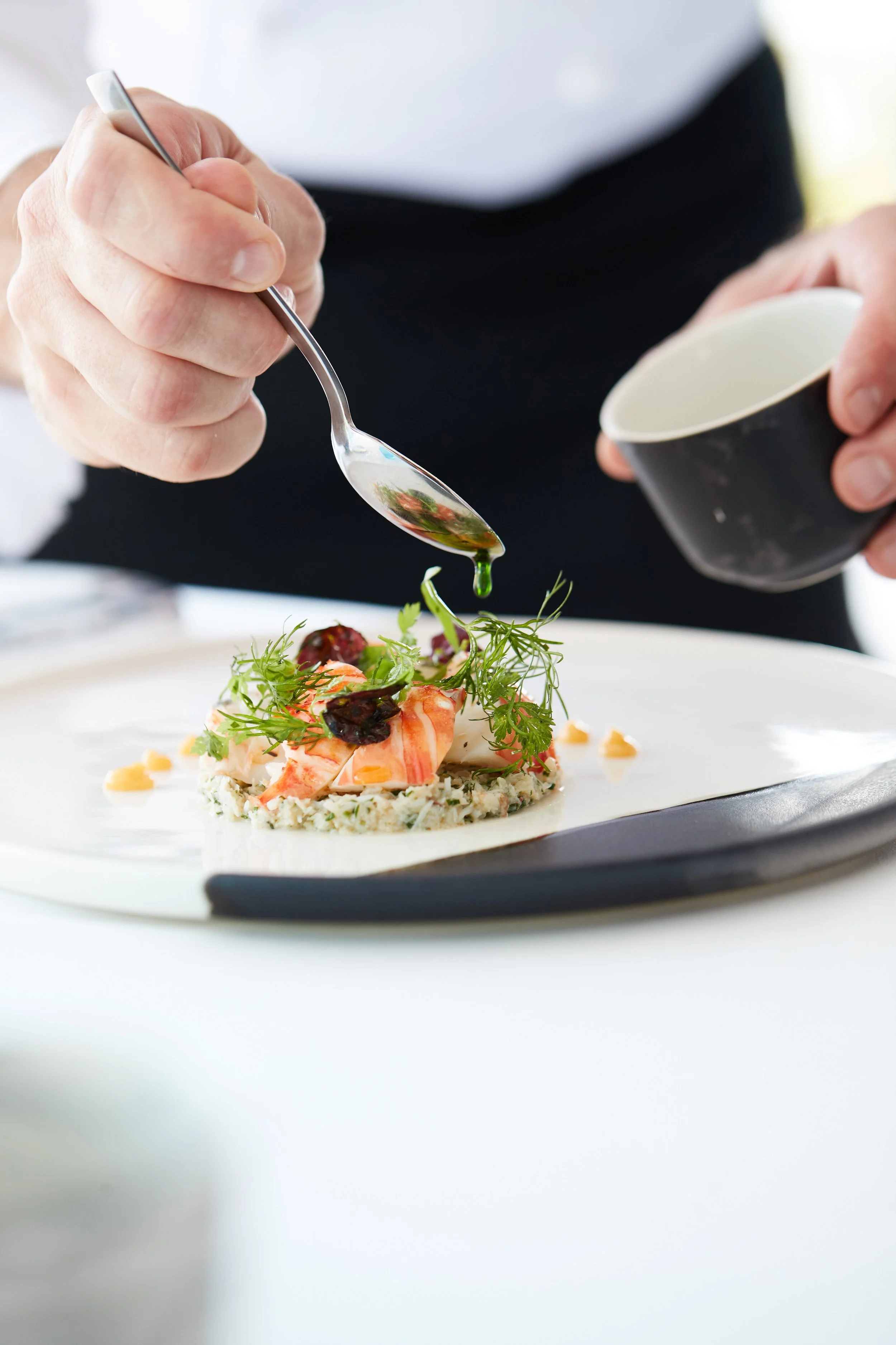 Chef drizzling sauce onto a plated gourmet appetizer with greens and vegetables.
