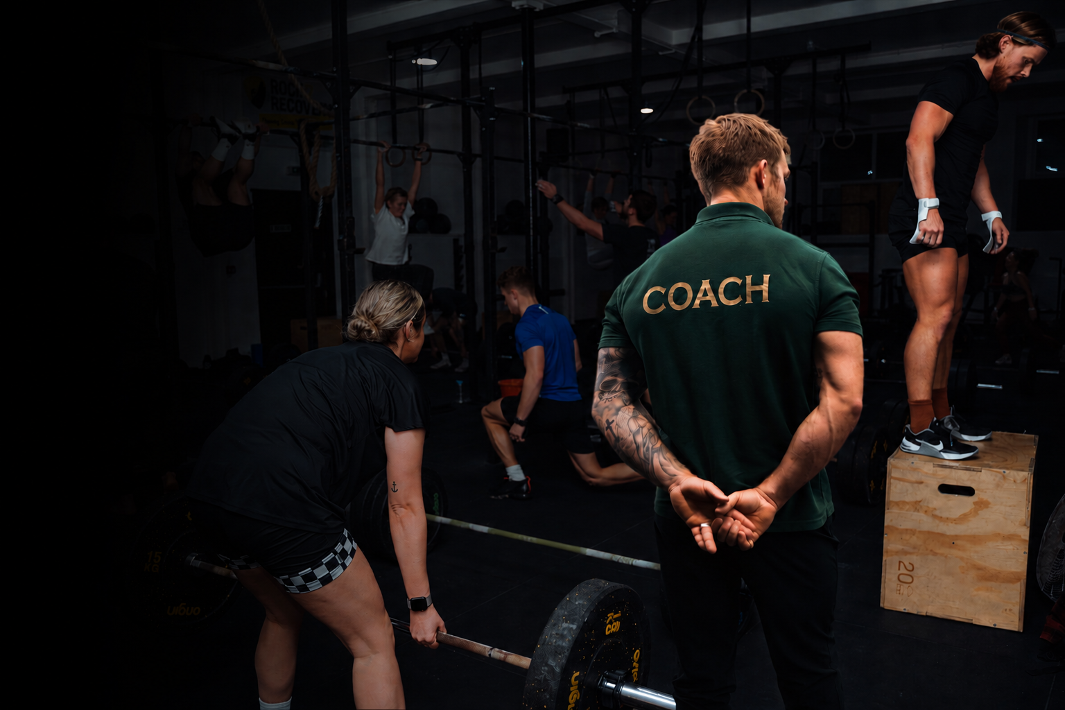 Pantheon Plymouth coach supervising a group functional fitness and strength training session, with members performing barbell lifts, gymnastics movements and conditioning exercises in a supportive gym environment.
