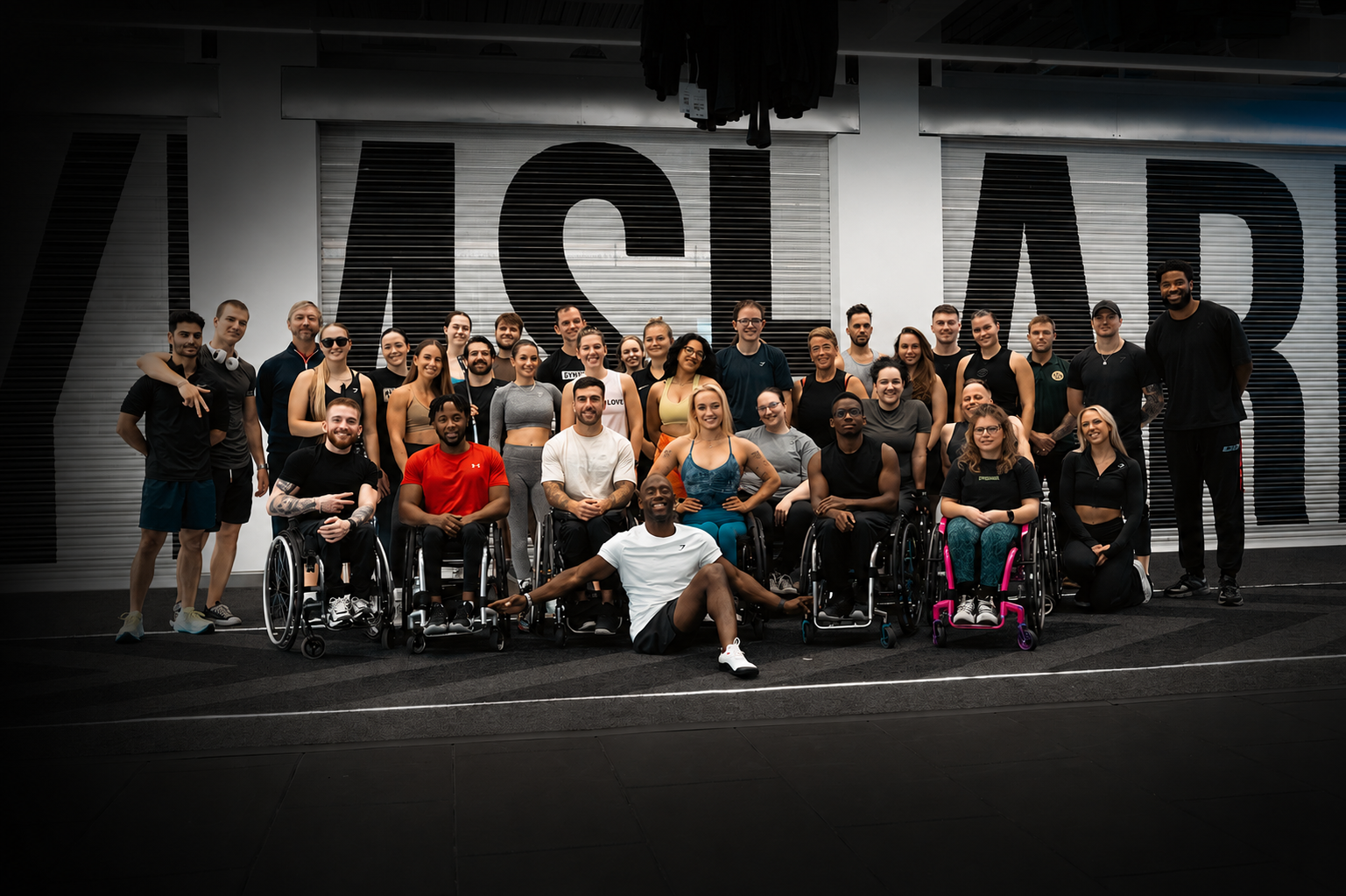 Group photo of Pantheon Plymouth members and coaches participating in an inclusive mixed-ability fitness community, featuring wheelchair users and non-disabled members training together in an accessible gym environment.