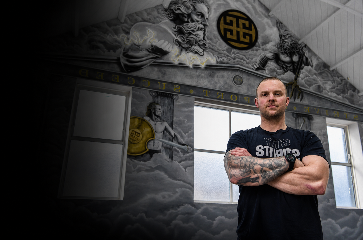 Founder and coach at Pantheon Plymouth standing confidently in the gym beneath the iconic Pantheon mural. Inclusive hybrid gym in Plymouth offering CrossFit, HYROX, personal training, adaptive training and fitness education.