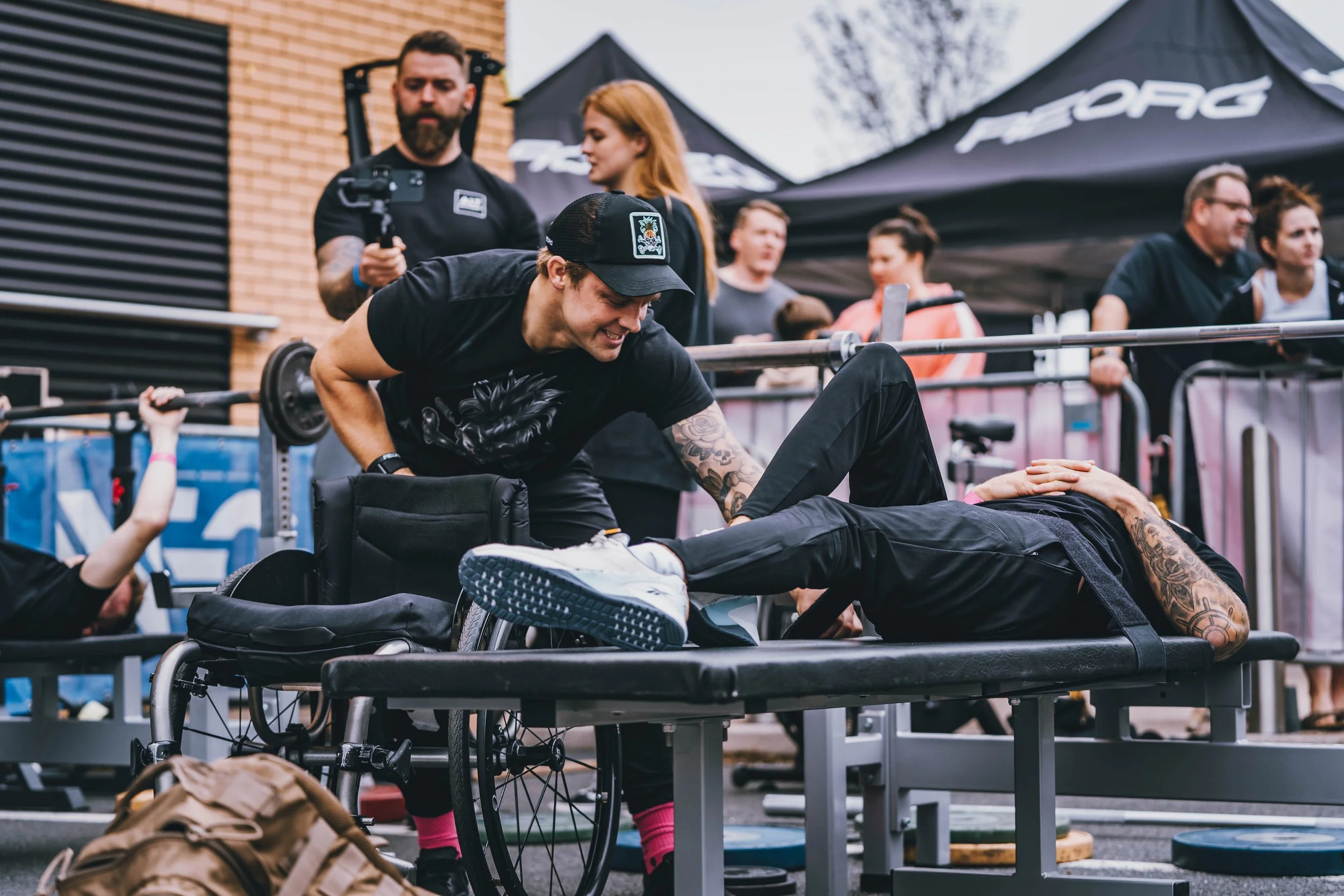 Coach supporting an adaptive athlete during a strength training event, demonstrating inclusive fitness and disability sport coaching.