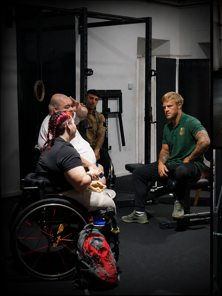 Alt text: Pantheon Plymouth coach leading an adaptive fitness consultation with wheelchair users in an accessible gym environment, discussing personalised training modifications and inclusive exercise options.