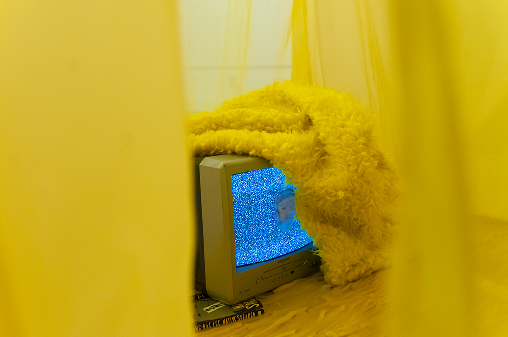  Is this | This is…  Multimedia installation: yellow curtains, old television, copy of Native Speaker by Chang Rae Lee, wig, 20 packs of rectangle dan moo ji, 5 packs of circle dan moo ji, print, shag rug, scrabble letters.  120” x 240” x 240”  Detai