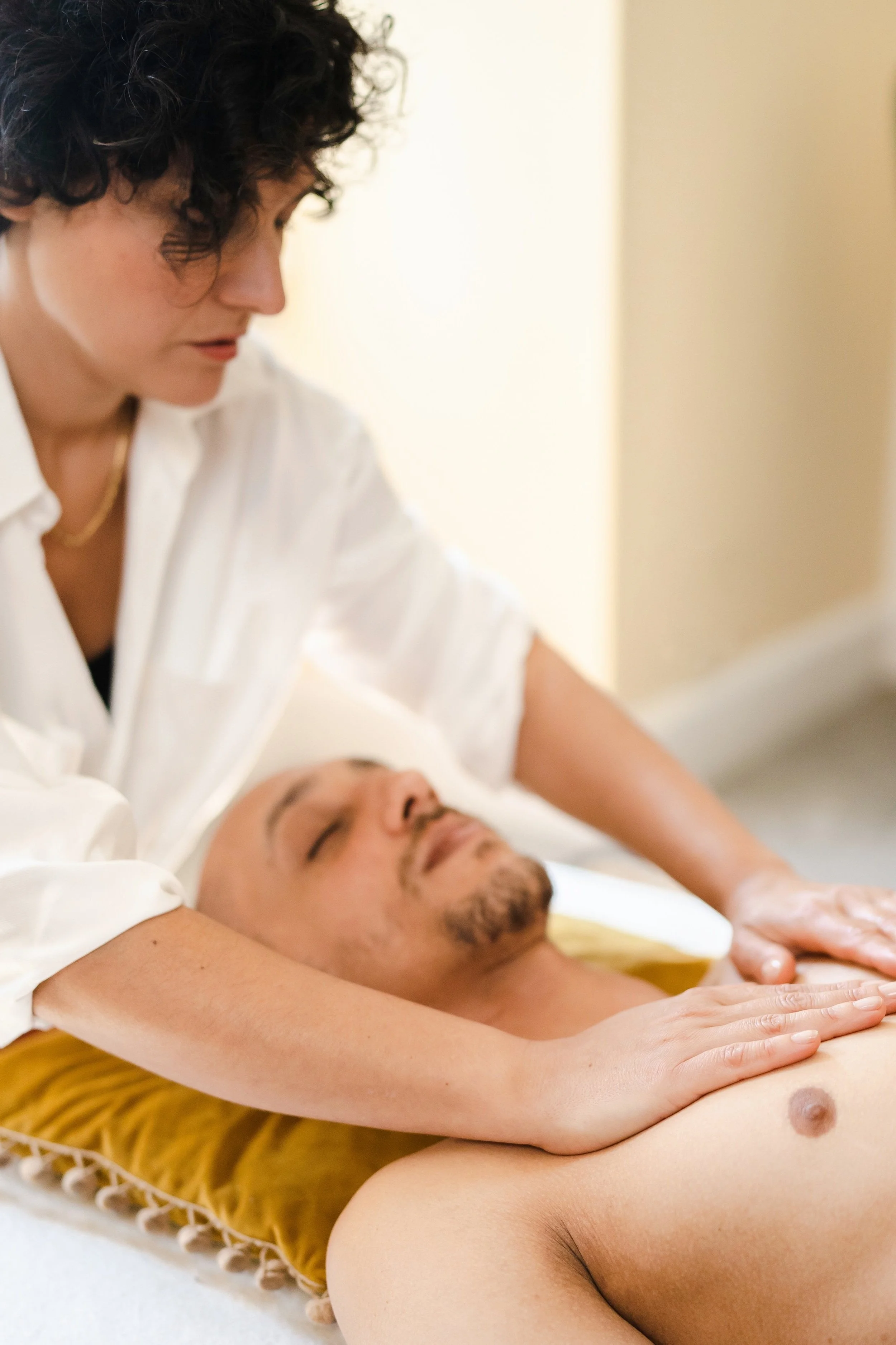 Person receiving a relaxing massage from a therapist in a white shirt, lying on a yellow pillow.