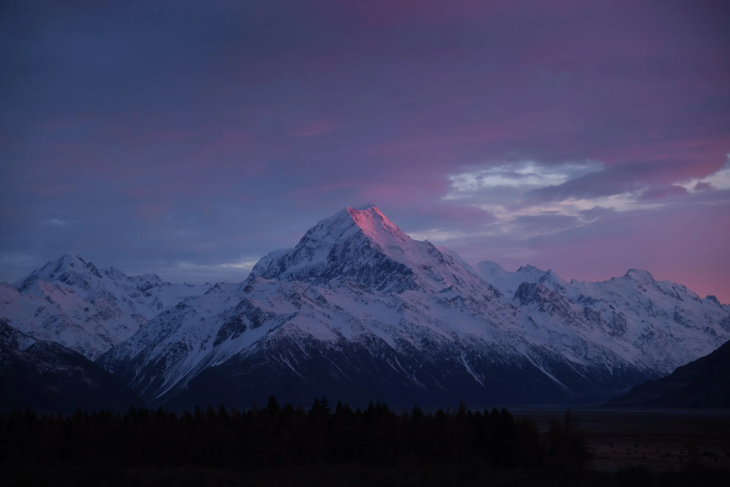 Snow-covered mountain peaks at dawn with a pink and purple sky.