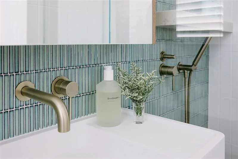 A stunning bathroom with gold tapware and a blue-green splashback