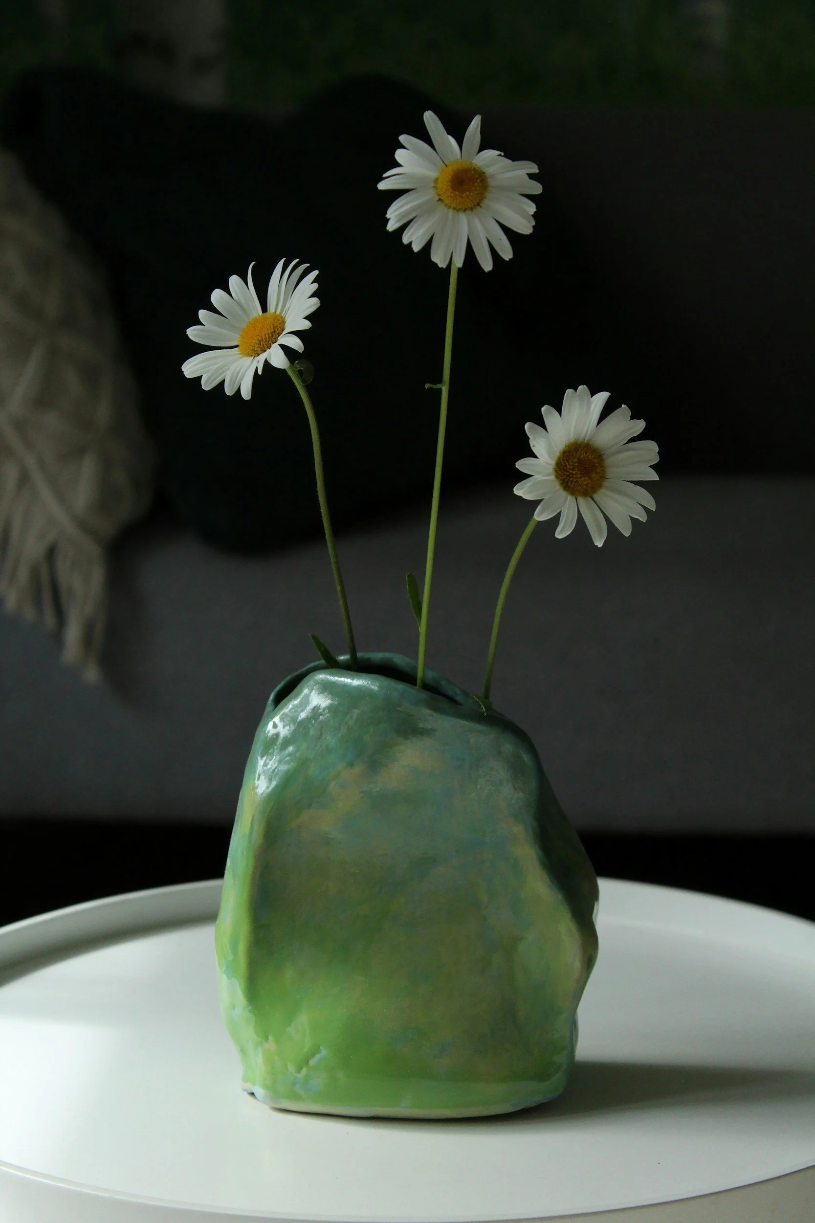 White daisies arranged in a green ceramic vase on a neutral surface