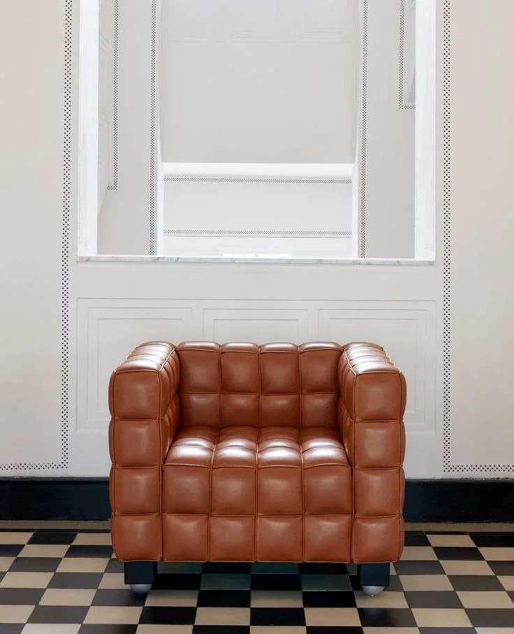 Red quilted-leather armchair in a sleek cube shape. It's set against white walls and a black and cream checkered floor.