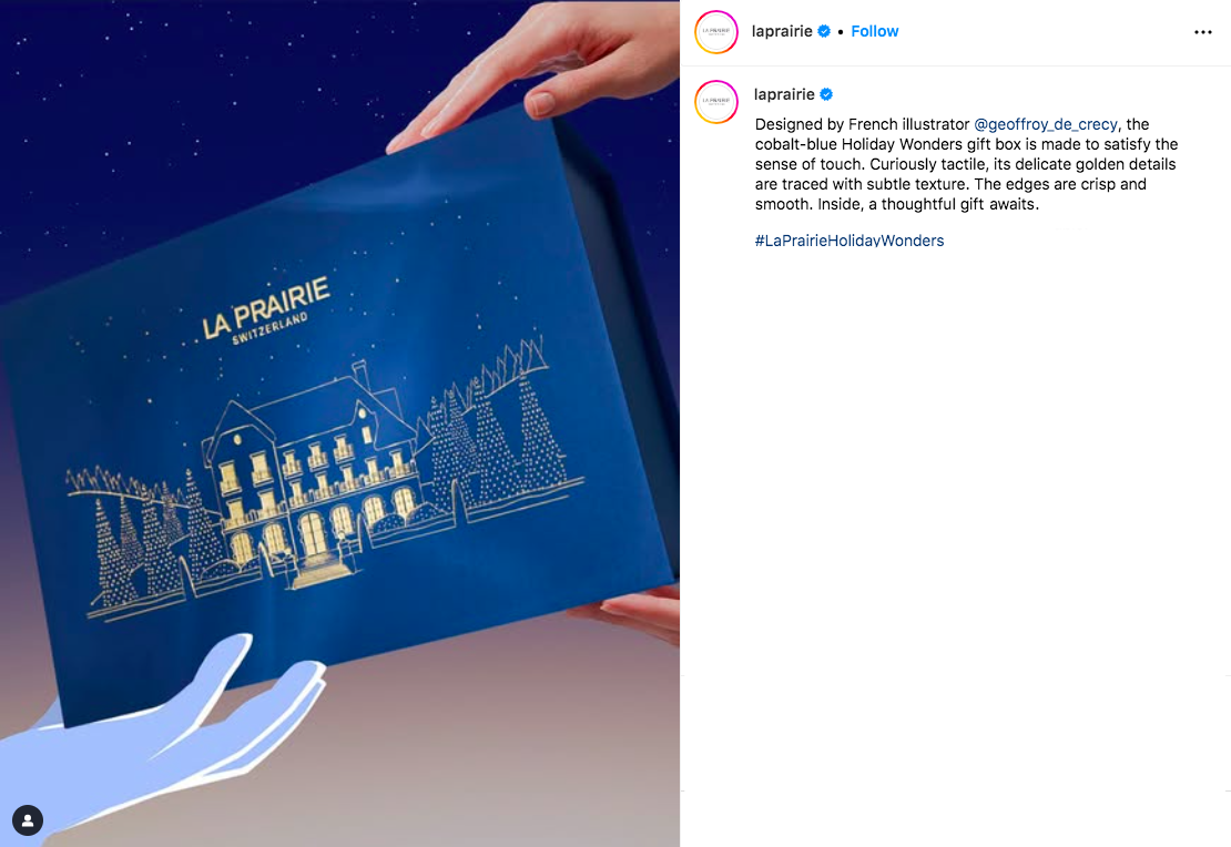 Animation frame of a blue gift box, with a gold festive illustration and starry night in the background, being handed over to someone. The hands are almost out of frame.