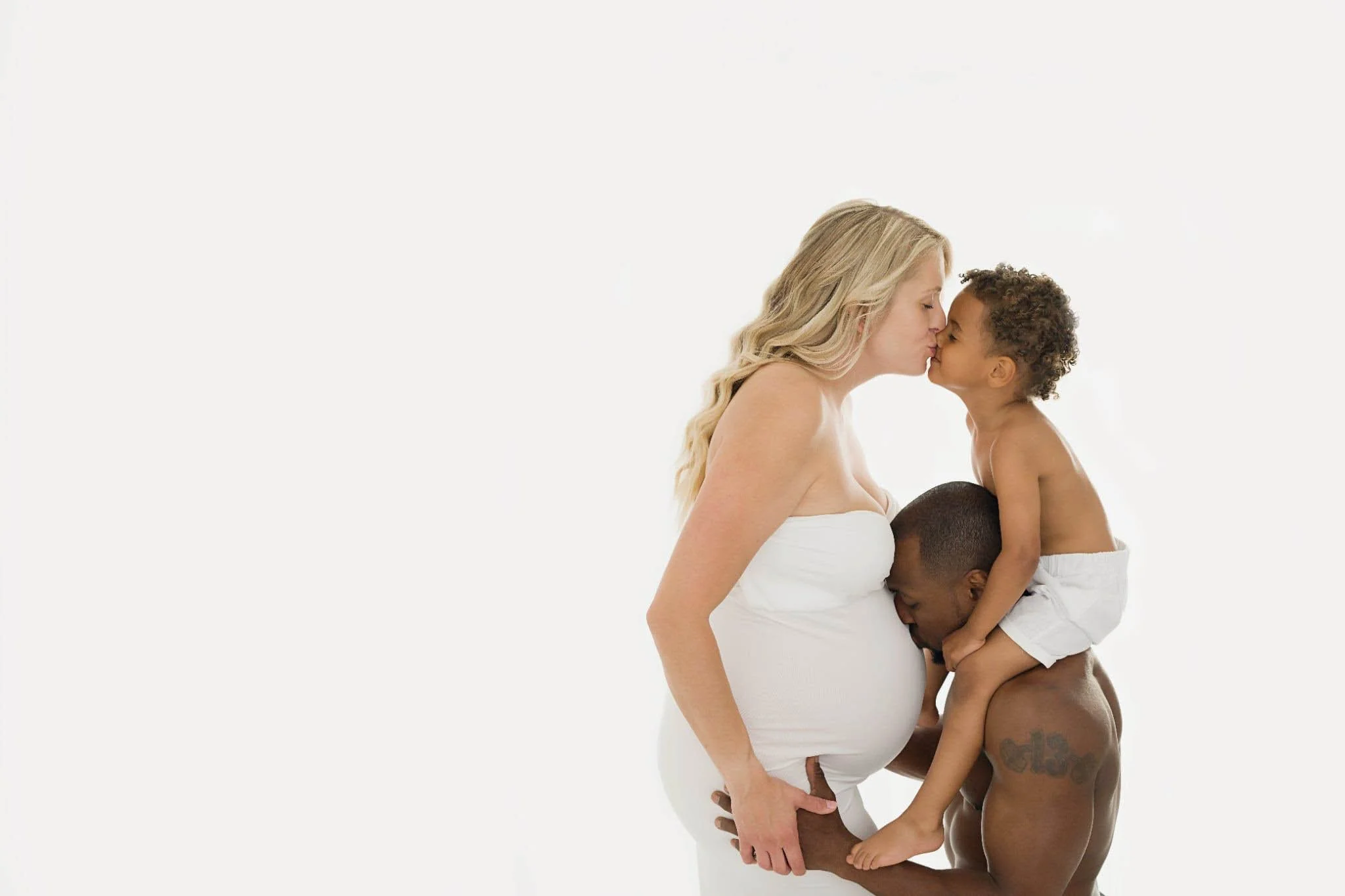 A woman with long blonde hair and a child with short curly hair are kissing and holding each other against a plain white background.