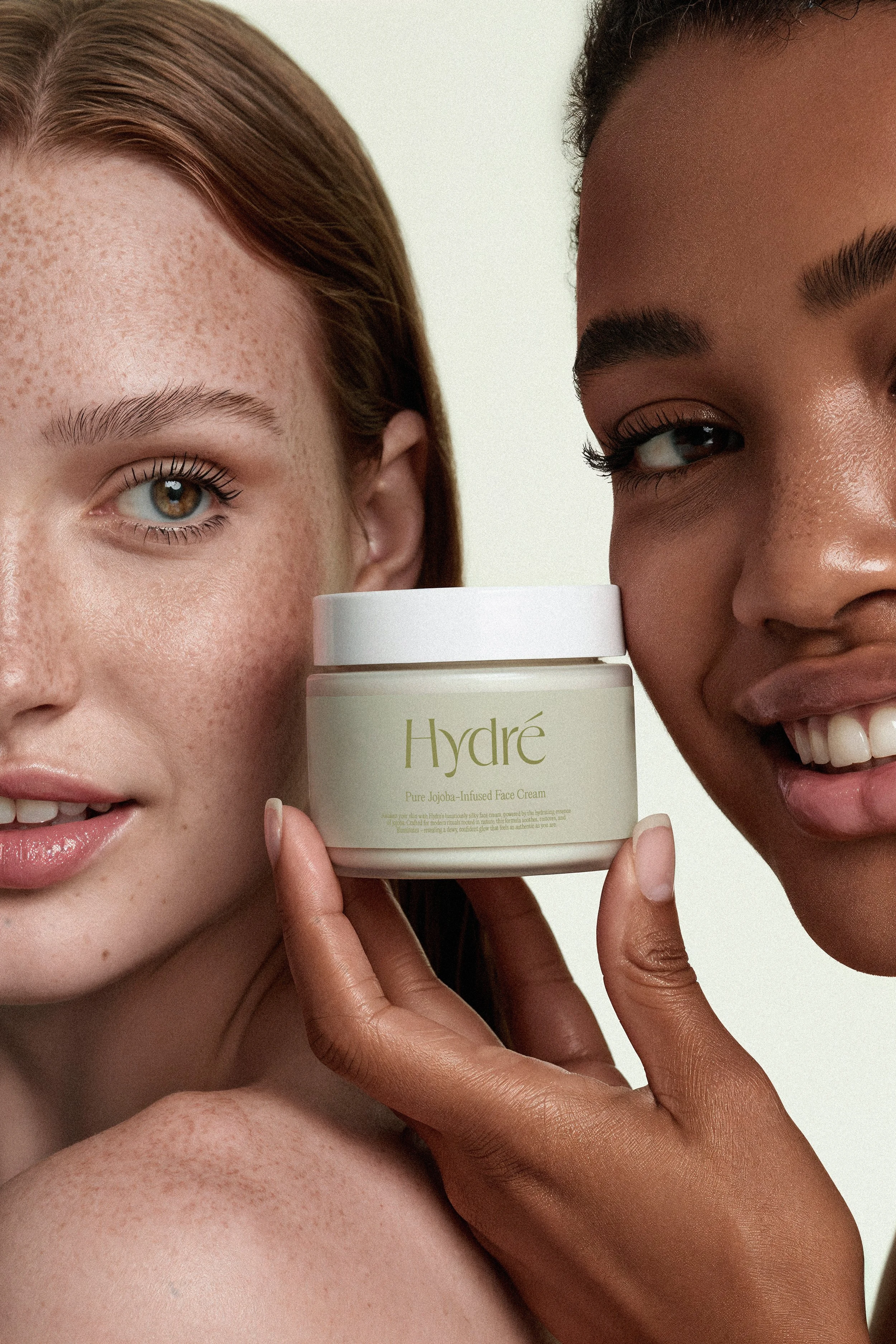 Two women with different skin tones holding a jar of Hydré face cream between them, close together, smiling partially visible.