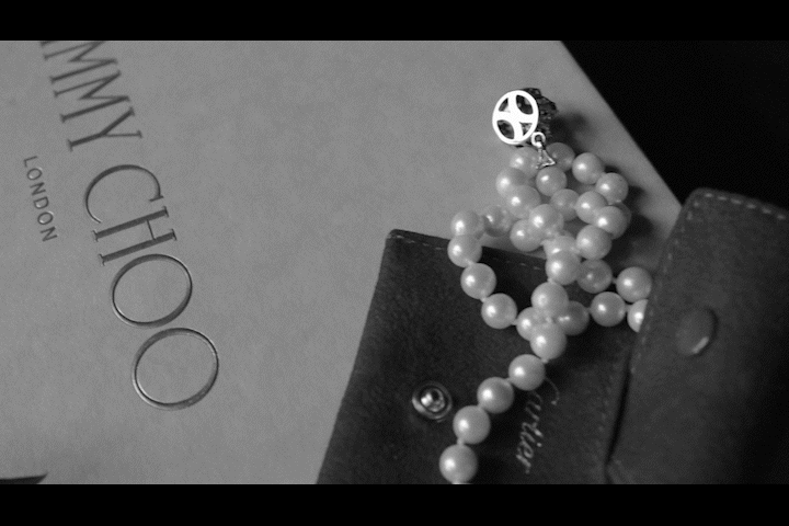 Perlenkette mit Anhänger auf einem schwarzen Ledergerät, neben einem Buch oder einer Zeitschrift mit gestempeltem Schriftzug.