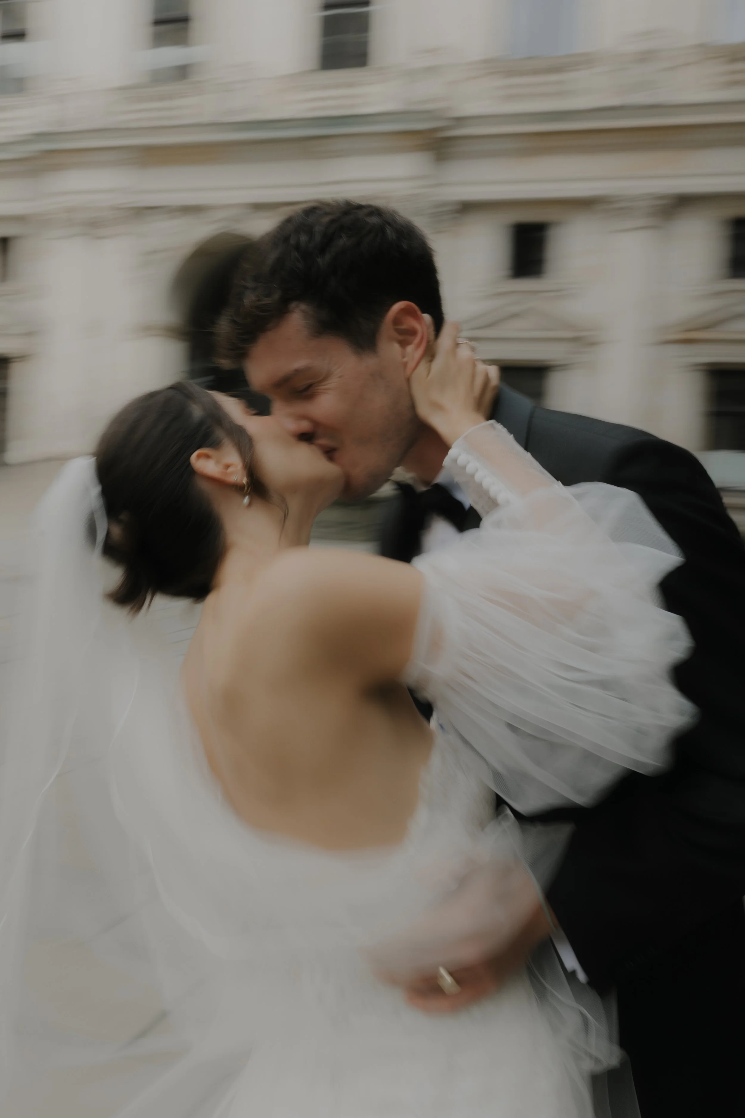 Ein frisch vermähltes Paar küsst sich leidenschaftlich vor einer historischen Gebäude.