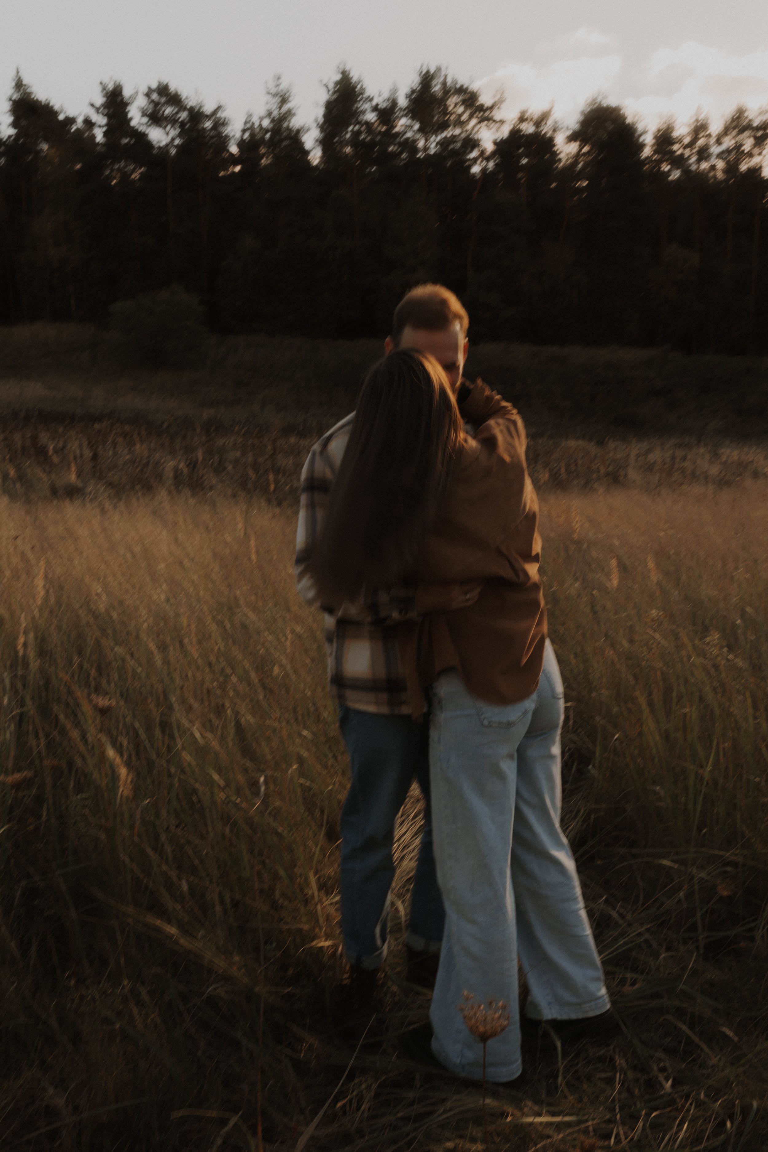 Zwei Menschen in einer Feldlandschaft bei Sonnenuntergang, die sich umarmen.